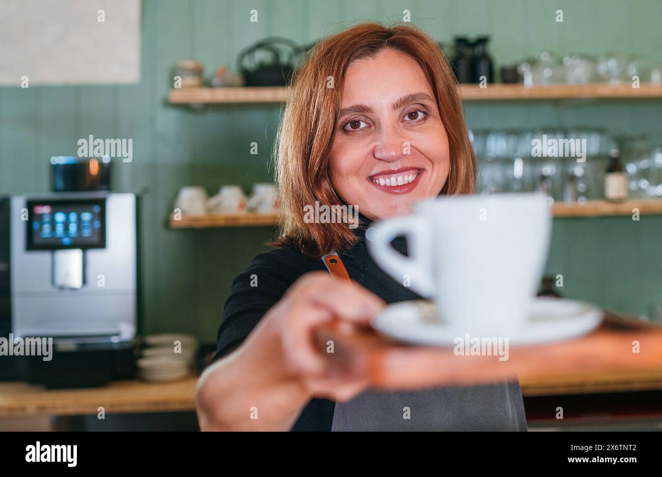 Fröhlich lächelnde Barista-Frau, die am Coffee Shop aromatischen Espresso mit weißer Tasse schenkt. Glückliche Menschen, Kaffeekonsum, Getränkeindustrie Stockfoto