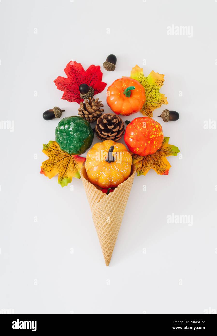 Eisbecher mit Herbstblättern, Kürbissen, Eicheln und Tannenzapfen auf weißem Hintergrund. Minimales kreatives Konzept für Sommer und Herbst. Idee für süßes Essen. Stockfoto