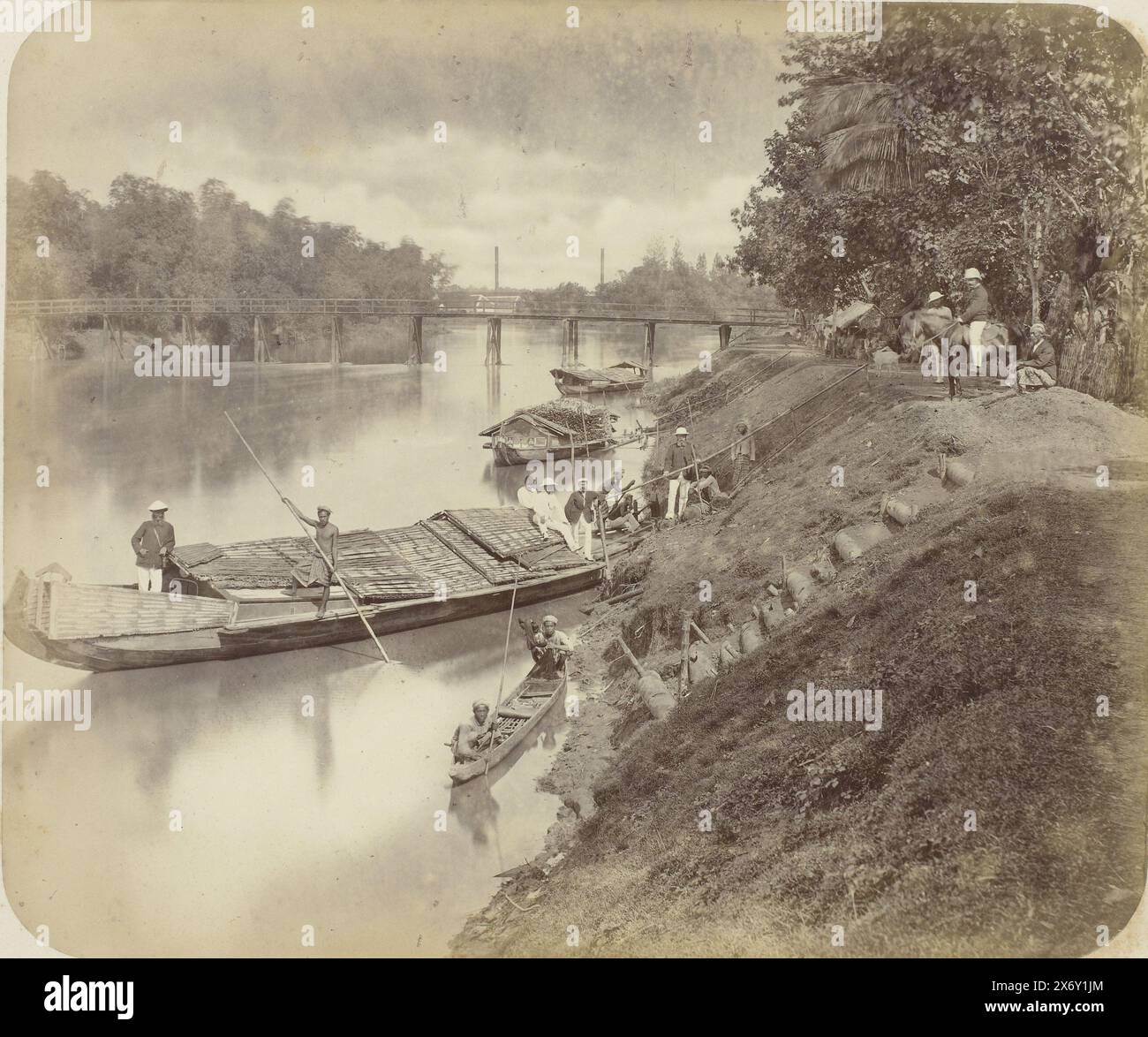 Die Kalibrantas in der Nähe von Surabaya, die Kalibrantas in der Nähe von Surabaya mit einem großen Kanu in der Mitte mit einem Javaner mit einem langen Segelstock und vorne ein Europäer mit einem Bart und einem Helm. Verschiedene javanische und Europäer an Land. Drei weitere Pirogen am Fluss und eine Holzbrücke im Hintergrund. In der Ferne zwei Schornsteinrohre. Teil des Fotoalbums, das von der Soerabayasche Association of Suikerfabrikanten an Frederik Beyerinck, Einwohner von Soerabaya, präsentiert wurde., Foto, Herman Salzwedel, Soerabayasche Vereeniging van Suikerfabrikanten, Surabaya, 1876 - 1884, fotografisch Stockfoto