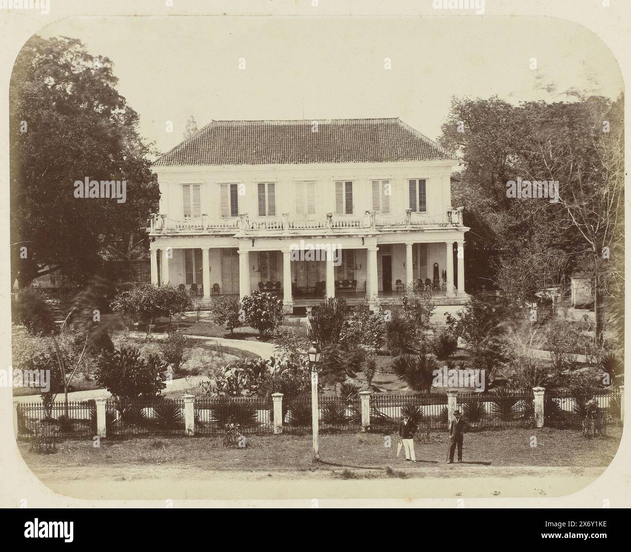 Das Residence House in Surabaya, das Residence House in Surabaya von vorne gesehen. Vor dem Haus gibt es einen großen Garten und eine große Veranda mit einer Reihe von Stühlen und einer Uhr auf der rechten Seite, die fünf nach zwei zeigt. Zwei Europäer stehen vor dem Tor auf der Straße. Teil des Fotoalbums, das von der Soerabayasche Association of Suikerfabrikanten an Frederik Beyerinck, Einwohner von Soerabaya, präsentiert wurde., Foto, Herman Salzwedel, Soerabayasche Vereeniging van Suikerfabrikanten, Surabaya, 1876 - 1884, fotografische Unterstützung, Albumendruck, Höhe, 22,3 cm x Breite, 27,8 Stockfoto