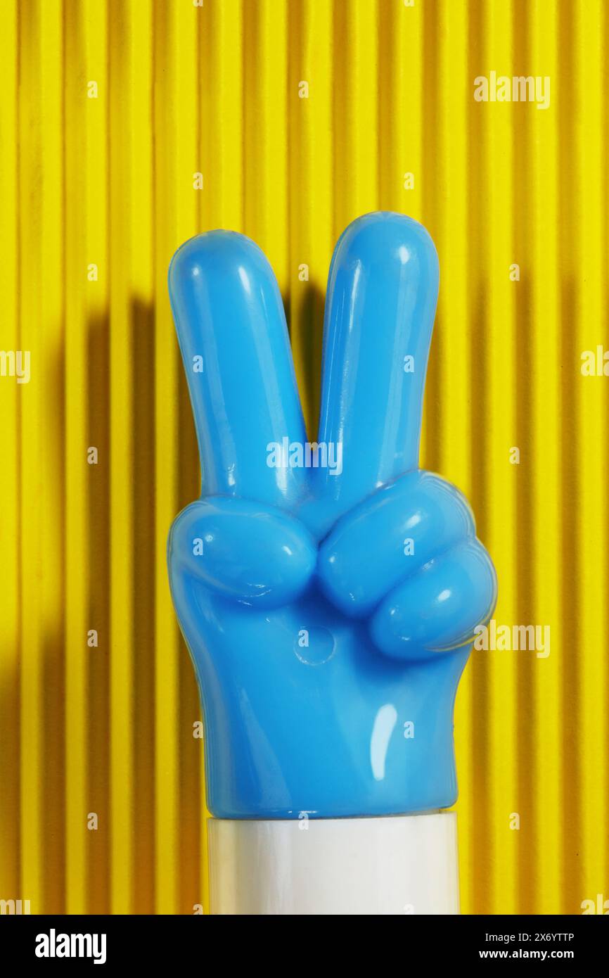 Zwei-Finger-Zeichen einer blauen Plastikspielzeug-Hand auf gelbem Hintergrund Stockfoto