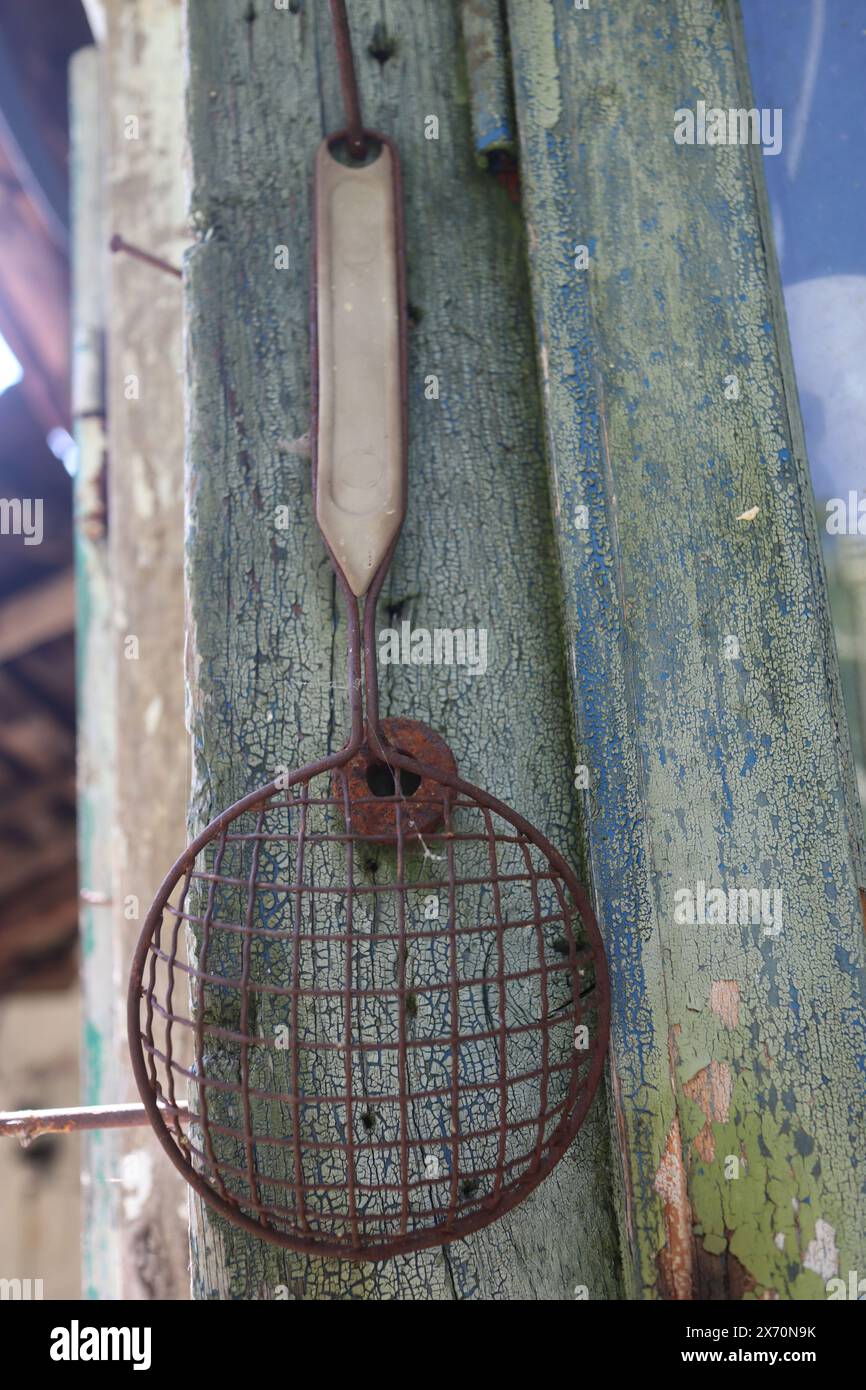 Sehr altes Sieb mit rostigem Griff, das an der Wand hängt Stockfoto