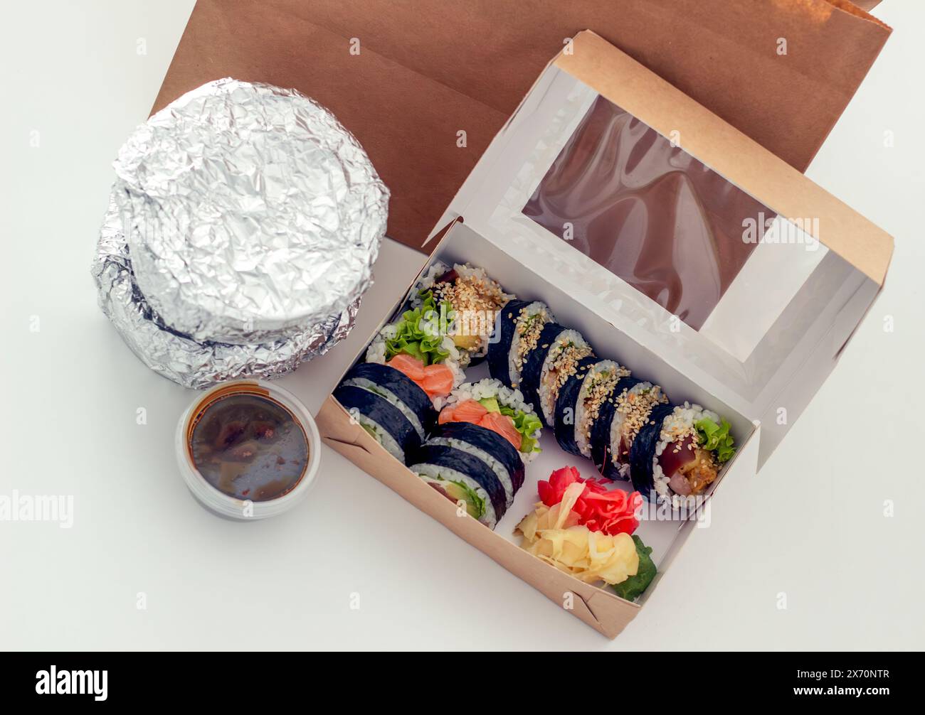 Sushi-Set auf einem weißen Tisch, Blick von oben, Behälter mit warmen Speisen in Folie und Sushi Stockfoto