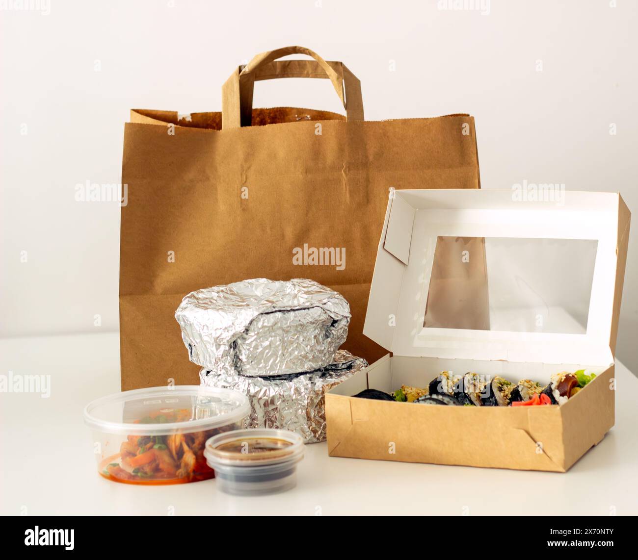 Sushi-Set auf einem weißen Tisch, Blick von oben, Behälter mit warmen Speisen in Folie und Sushi Stockfoto