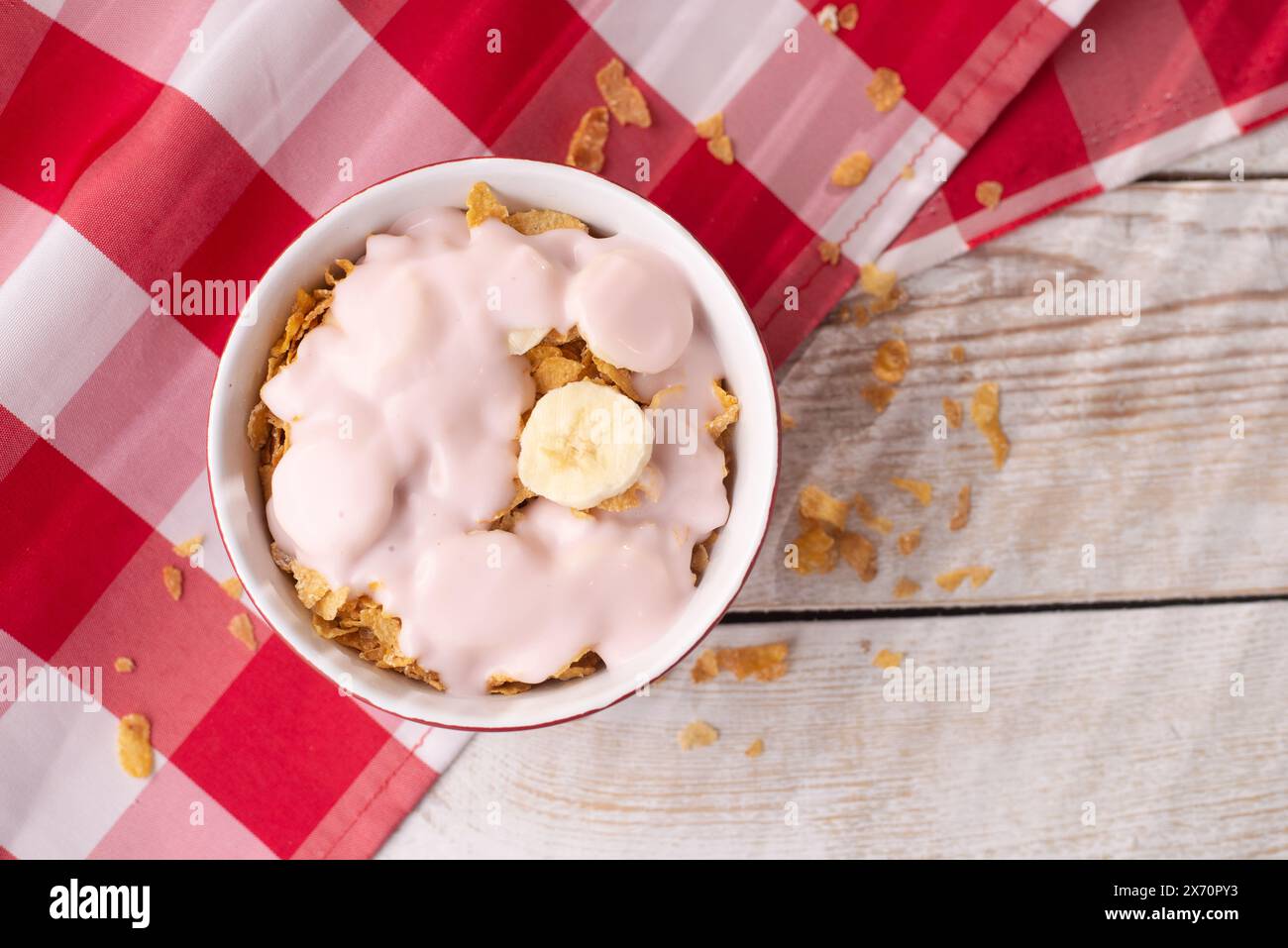 Gesundes Frühstück. Müsli mit Joghurt und Banane auf hellem Holzhintergrund mit roter Tischdecke. Blick von oben. Kopierbereich Stockfoto