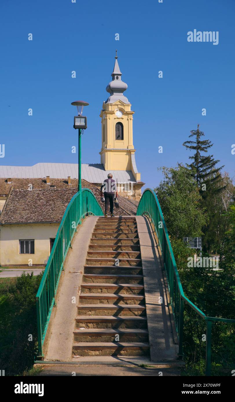 Alte Frau auf der Fußgängerbrücke zur St. Pauls Kirche in Bac, Vojvodina, Serbien Stockfoto