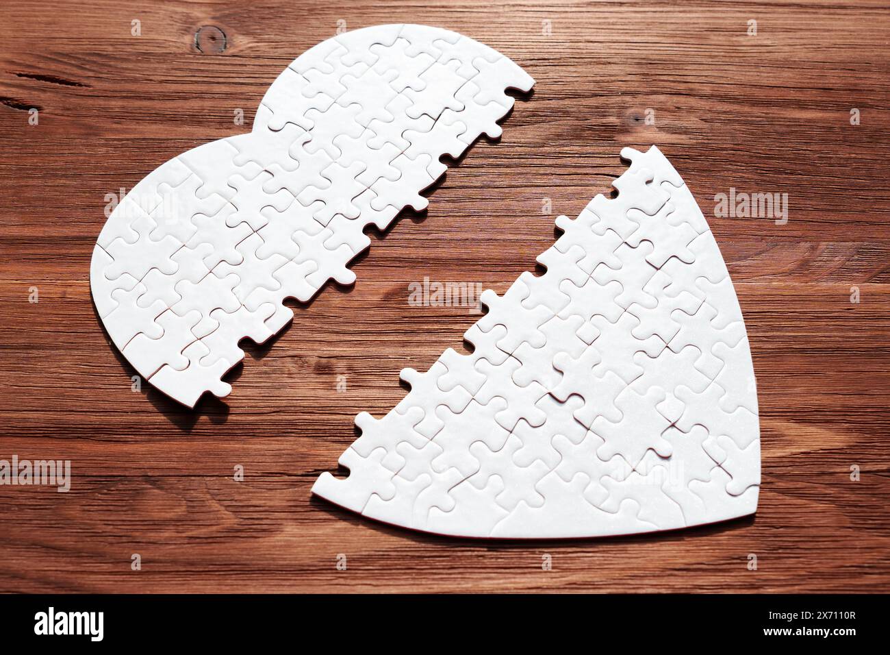 Eine Nahaufnahme eines weißen, herzförmigen Puzzles, das auf einem dunklen Holzhintergrund zerlegt liegt. Liebe, Verlust und die Suche nach Vollendung. Stockfoto