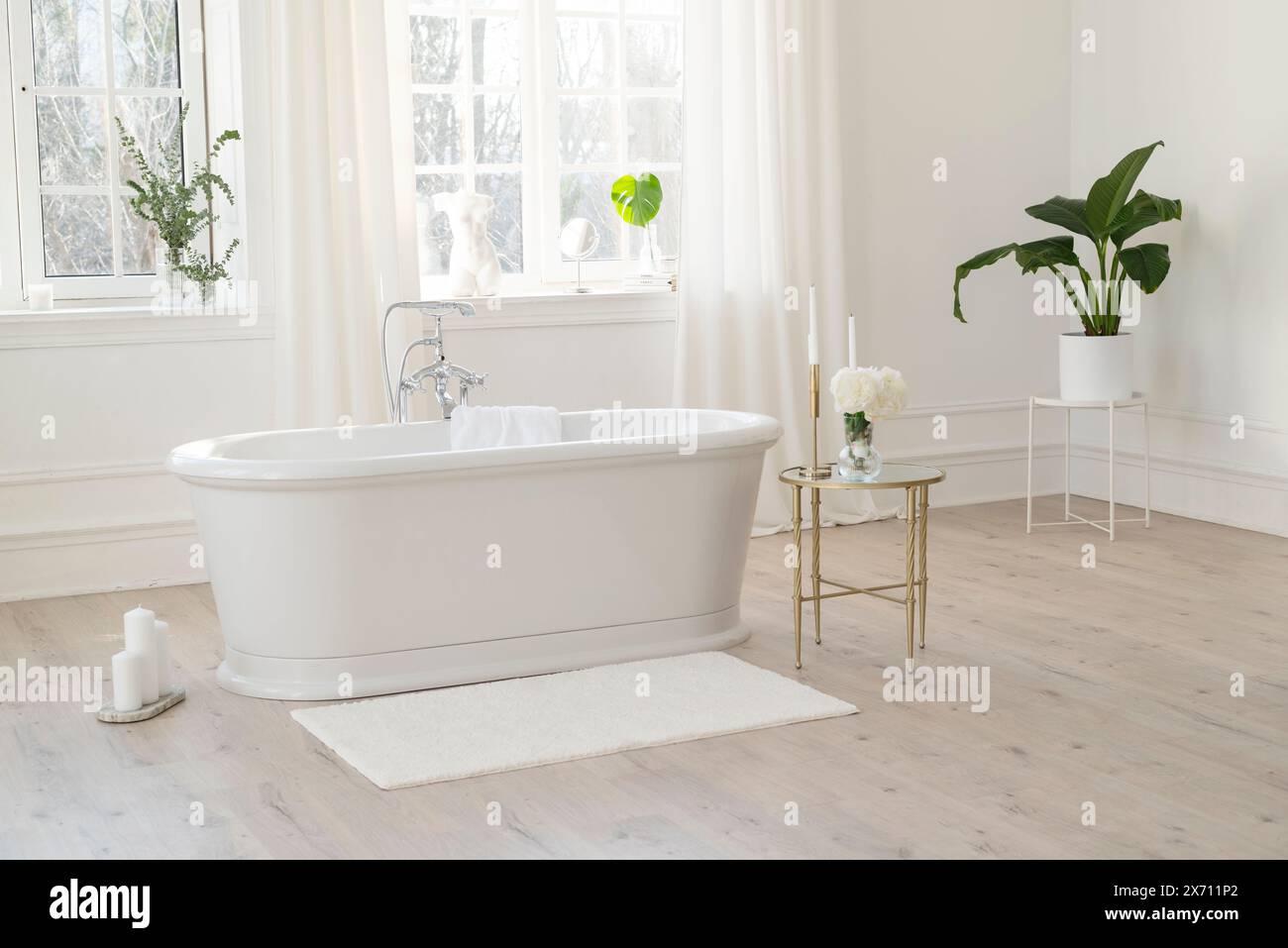 Weißes, modernes Badezimmer mit silbernen Armaturen, großen, sonnigen Fenstern, Dekorationen und Pflanzen. Innenraumkonzept. Weicher selektiver Fokus Stockfoto
