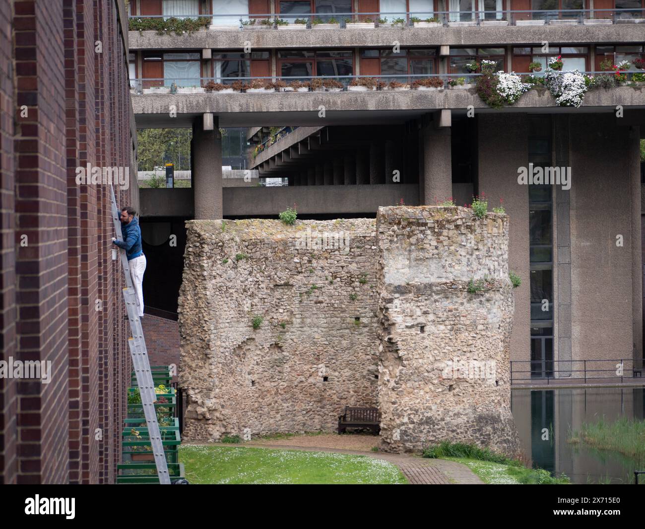 Handwerker befestigen Fenster auf dem Barbican-Anwesen London mit London Wall Bastion, im Hintergrund Stockfoto