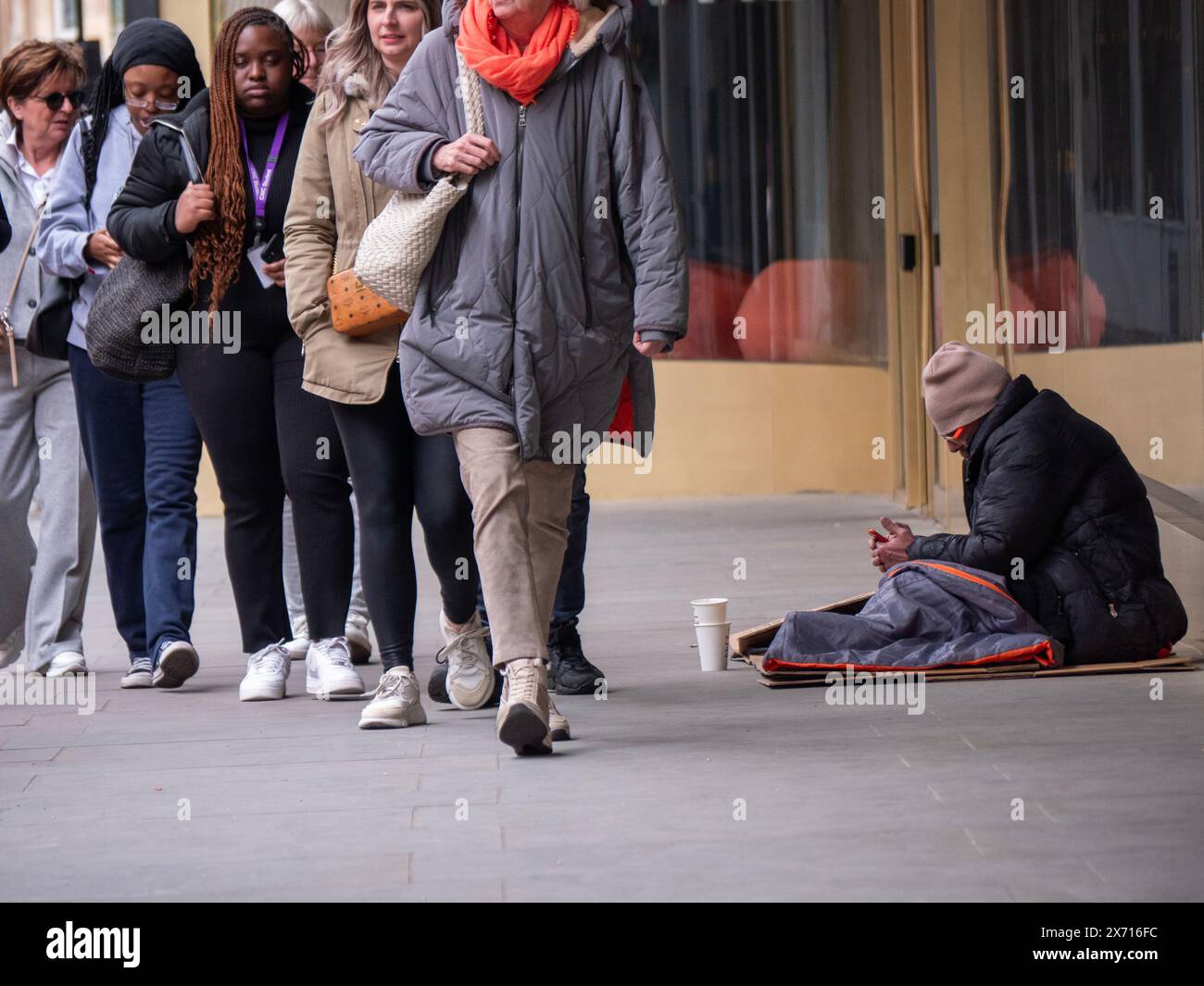 Obdachloser Mann im Schlafsack mit Handy unter den Menschenmassen von Einkäufern, Charing Cross Road London Stockfoto Obdachloser Mann im Schlafsack mit Handy unter den Menschenmassen von Einkäufern, Charing Cross Road London Stockfoto