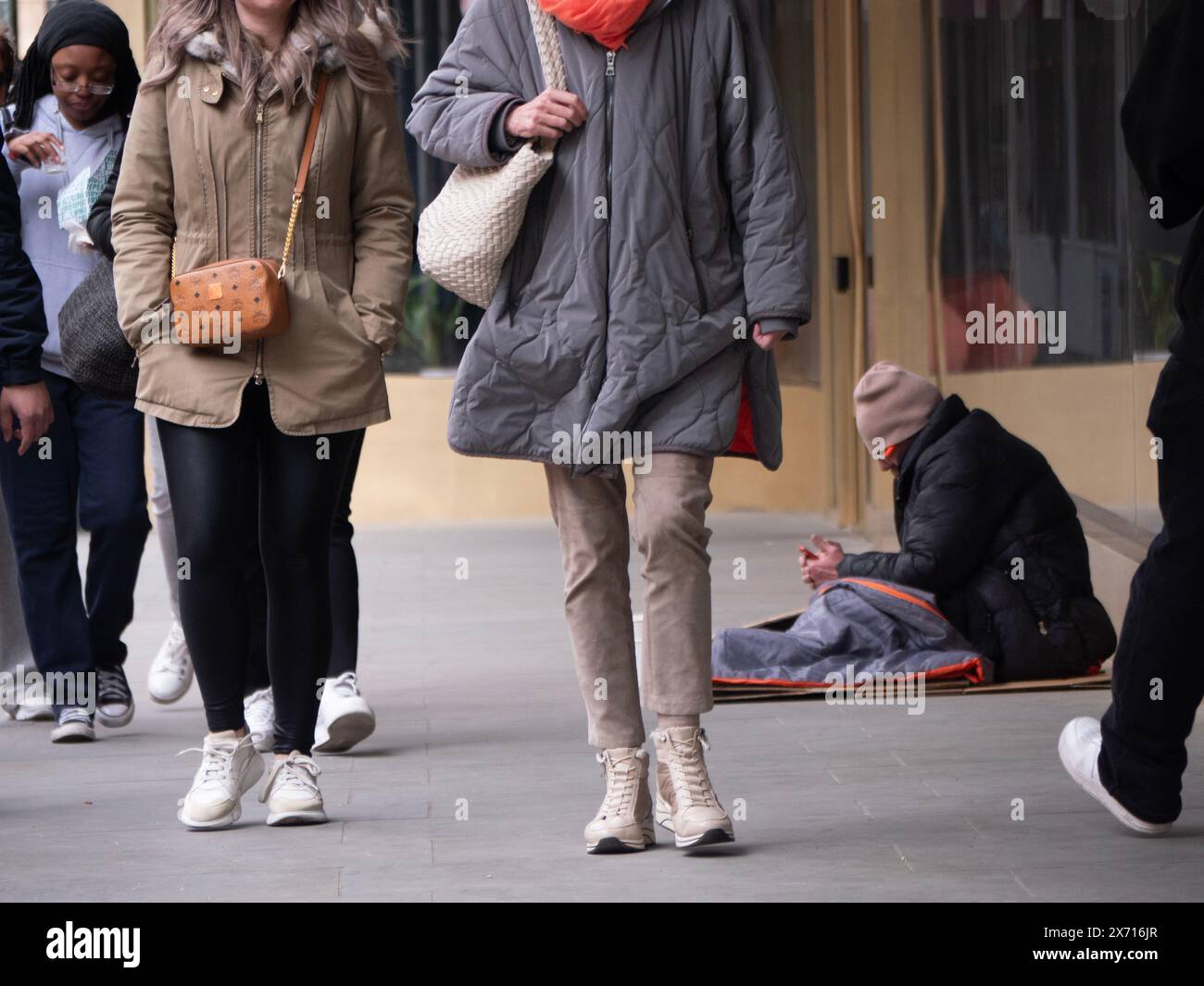 Obdachloser Mann im Schlafsack mit Handy unter den Menschenmassen von Einkäufern, Charing Cross Road London Stockfoto Obdachloser Mann im Schlafsack mit Handy unter den Menschenmassen von Einkäufern, Charing Cross Road London Stockfoto