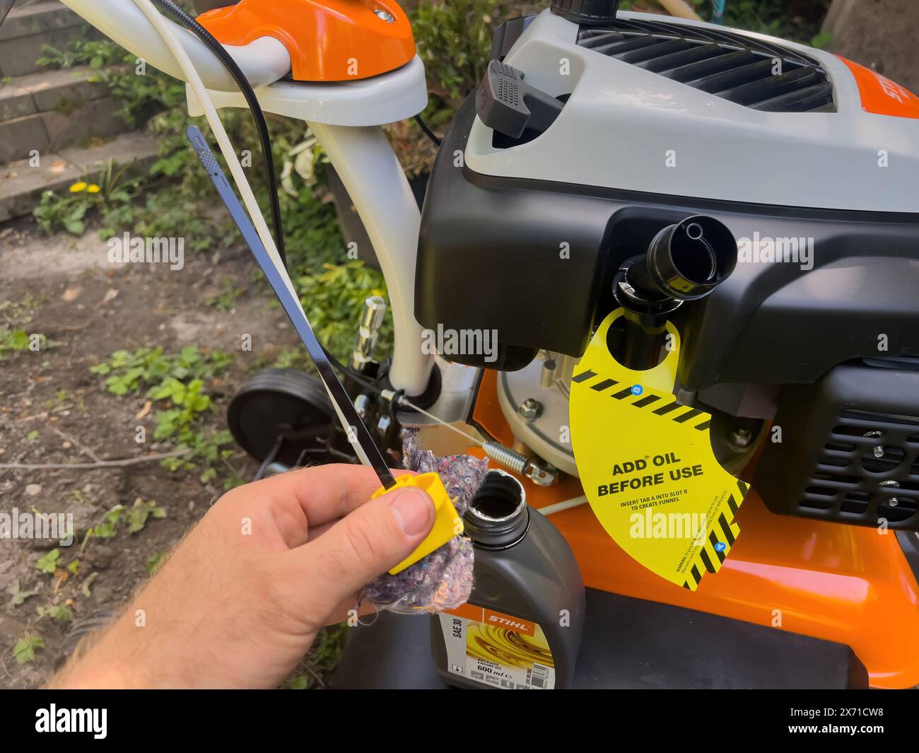 Frankfurt, Deutschland - 4. Mai 2023: Eine Hand, die einen Ölmessstab neben einer Stihl Gartenhacke hält, mit einem gelben Aufkleber Öl vor Gebrauch hinzufügen sichtbar, um die Motorhacke für die erste Verwendung im Garten vorzubereiten Stockfoto