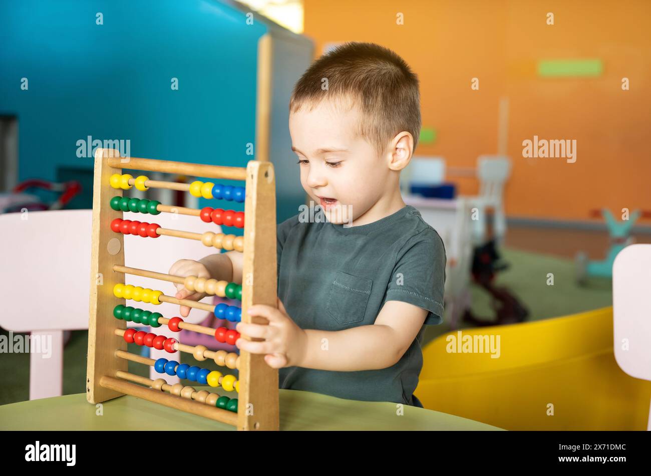 Lächelnder Kleinkind, der mit farbenfrohen Spielzeugabakus in einem Kinderunterhaltungs-Center spielt. Lernspielzeug für Kinder. Stockfoto