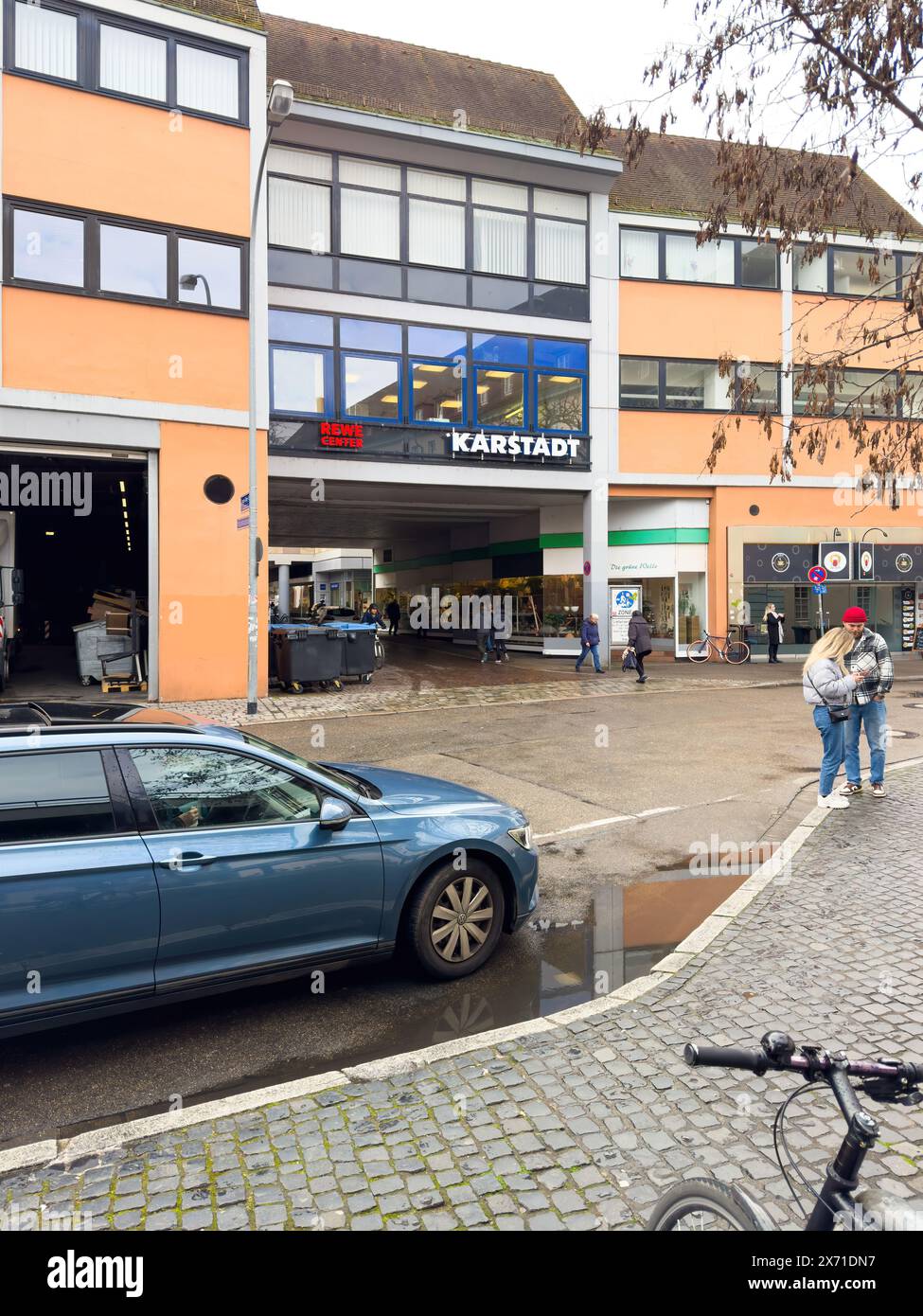 Freiburg - 6. März 2024: Ein VW Passat parkt in der Nähe des Rewe-Zentrums und der Karstadt in einer deutschen Stadt. Ein paar Fußgänger gehen im Hintergrund, um die typische urbane Szene hervorzuheben. Stockfoto