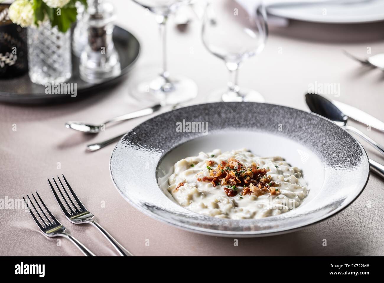Halusky als traditionelle slowakische Kartoffelgnocchi mit Schafskäse Bryndza, gebratenem Speck und Schnittlauch serviert auf einem modernen Teller und in einem festlich gedeckten Restaurant Stockfoto