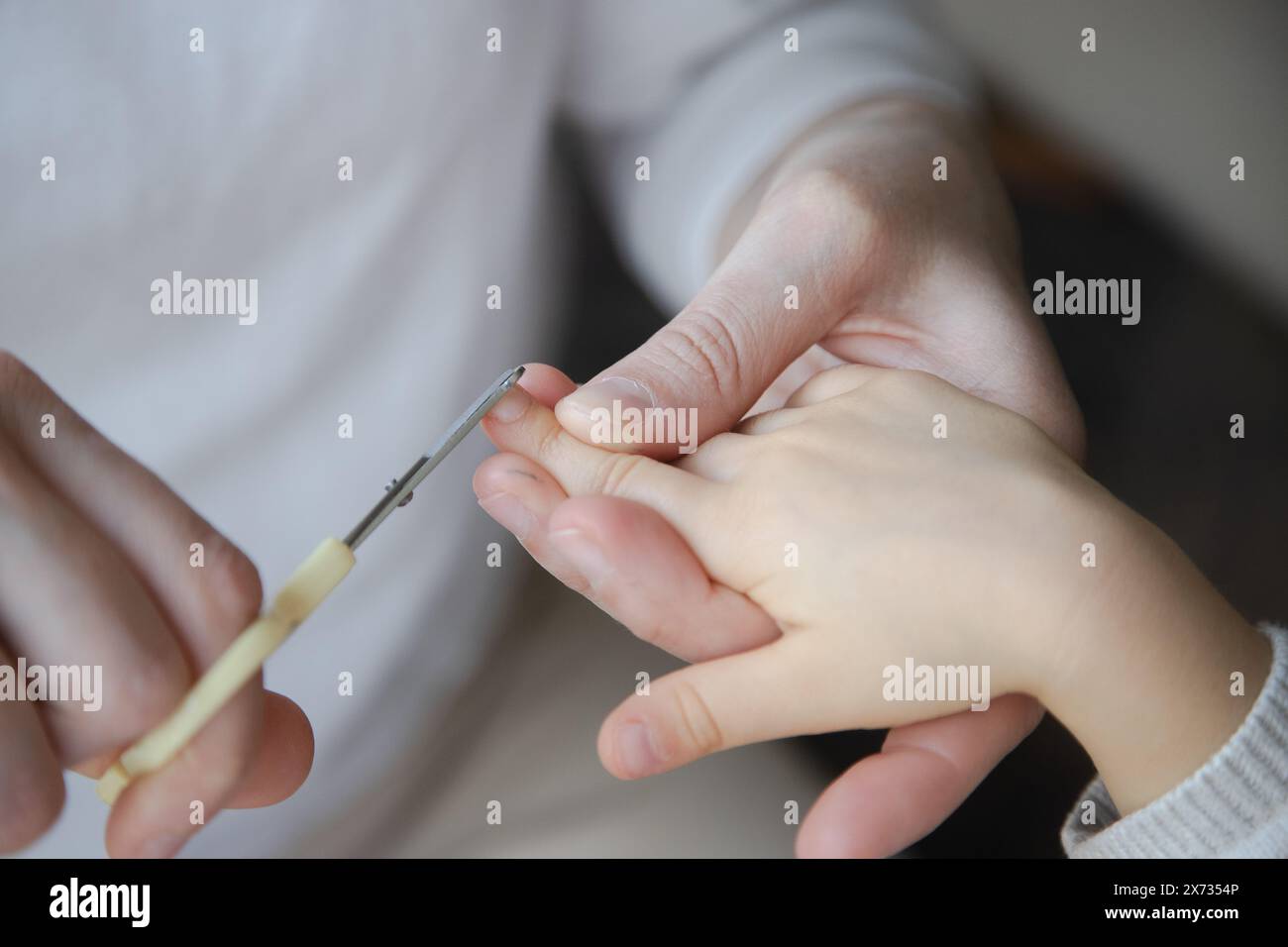 Nahaufnahme eines Erwachsenen, der die Fingernägel eines Kindes sorgfältig trimmt, um einen zarten Moment der Pflege und Pflege hervorzuheben. Stockfoto