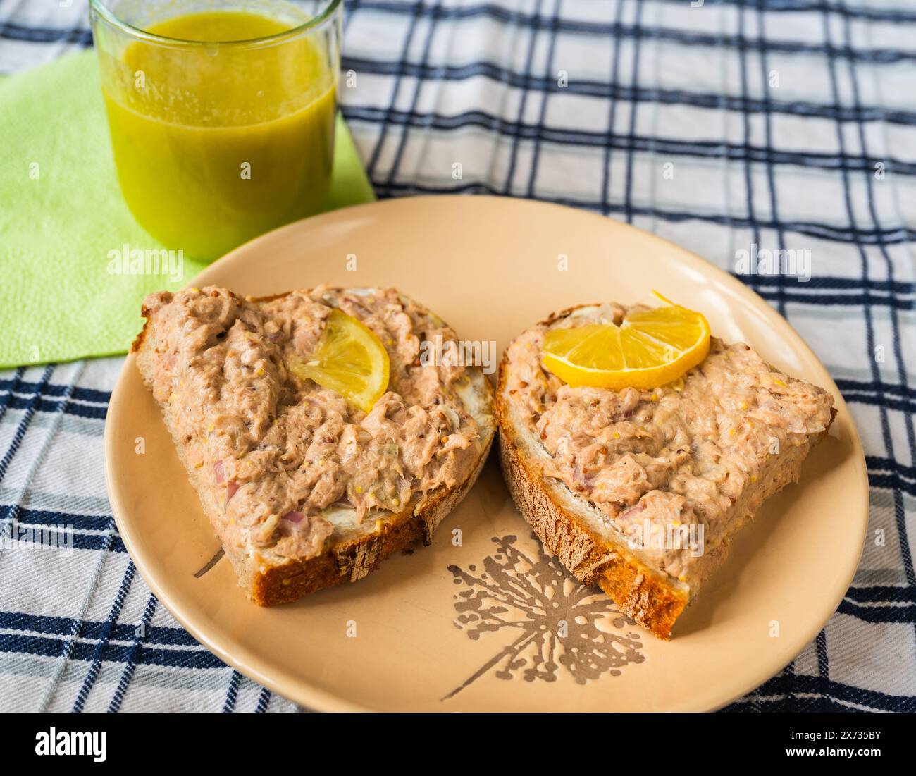 Zwei Scheiben Brot mit Thunfischaufstrich, Zitrone, grüner Smoothie im Glas auf dem Tisch, Nahaufnahme. Frühstück oder Snack. Stockfoto