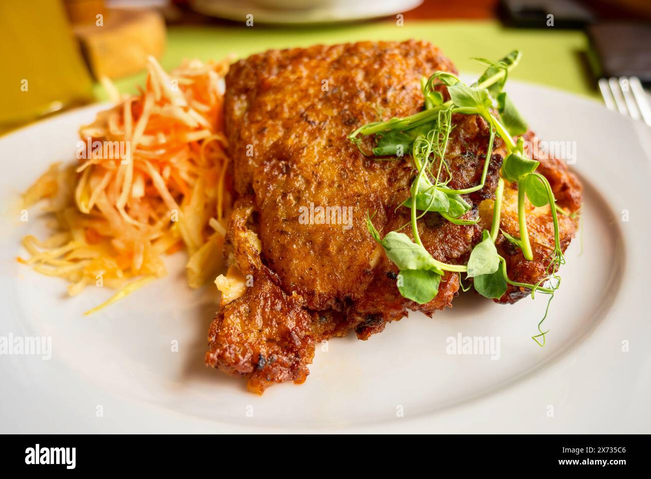 Gebratenes Schweinefleisch in Kartoffelteig, Karotten- und Kohlsalat, gekeimtes Erbsenblatt auf weißem Teller auf dem Tisch. Stockfoto