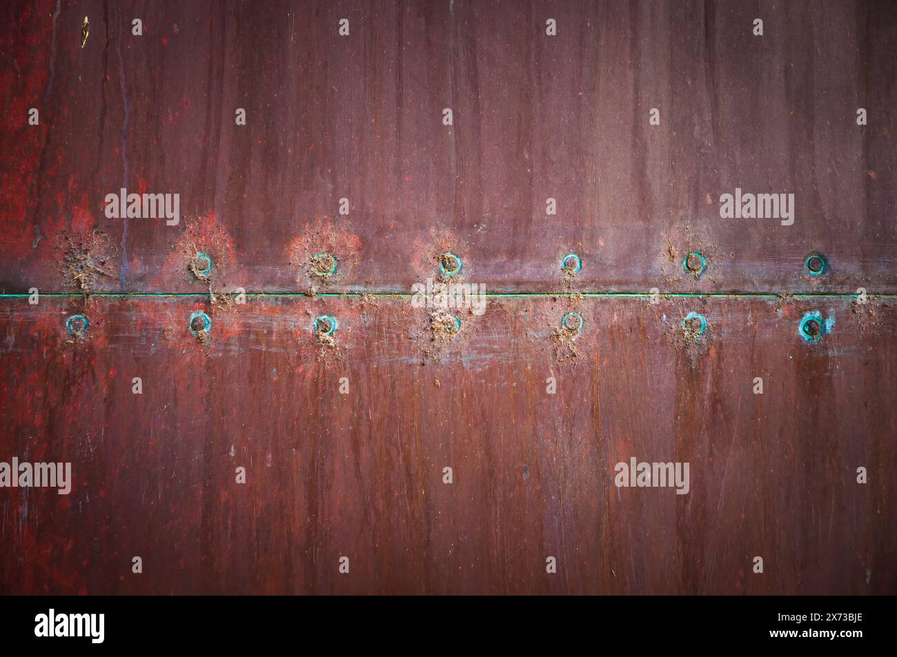 Detail einer rostfarbenen Blechtür, strukturiert, geprägt und in rötlichen Tönen. Stockfoto