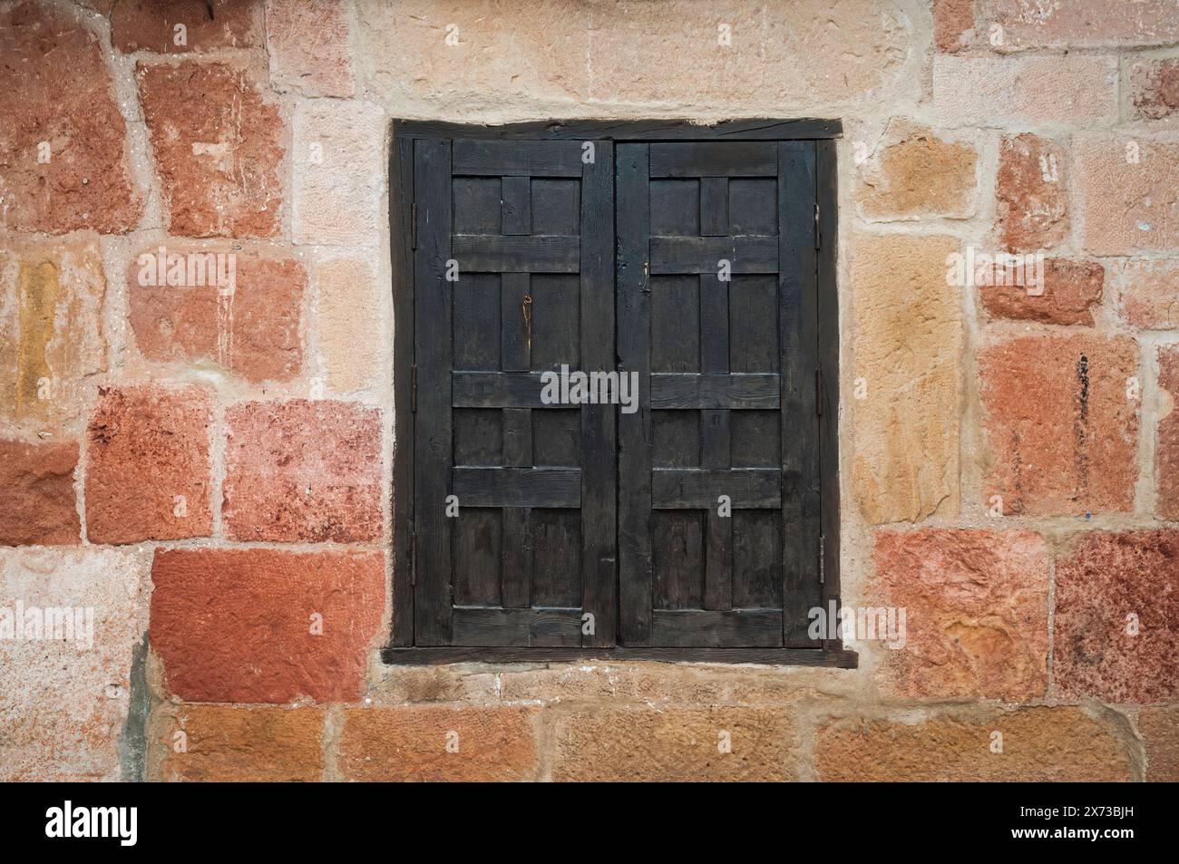 Detail der Fassade mit Steinmauer in warmen Tönen und einem geschlossenen schwarzen Holzfenster in der Mitte. Stockfoto Detail der Fassade mit Steinmauer in warmen Tönen und einem geschlossenen schwarzen Holzfenster in der Mitte. Stockfoto