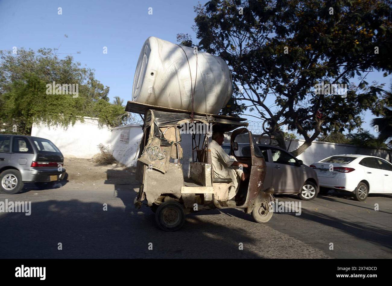 Ein Rikscha-Fahrer trägt einen riesigen Wassertank auf seiner Rikscha, der am Freitag, den 17. Mai 2024, in Do Talwar in Karachi eine Straße durchquert, die gegen die Verkehrsregeln verstößt. Quelle: Pakistan Press International (PPI)/Alamy Live News Stockfoto