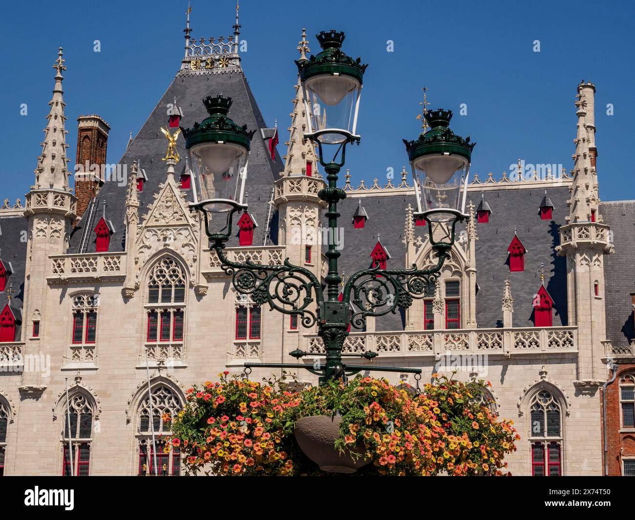 Gotisches historisches Gebäude unter blauem Himmel, mit dekorativer Laterne und Blumen im Vordergrund, prächtiges historisches Gebäude mit einer Laterne Stockfoto