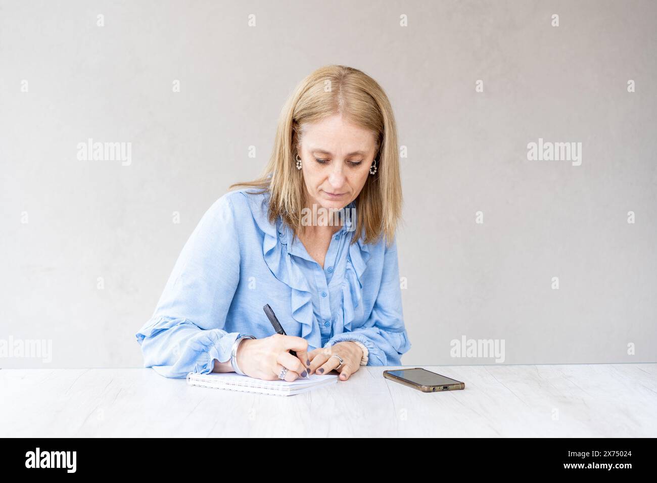 Die schöne Frau im mittleren Erwachsenenalter schreibt in ihr Notizbuch Stockfoto