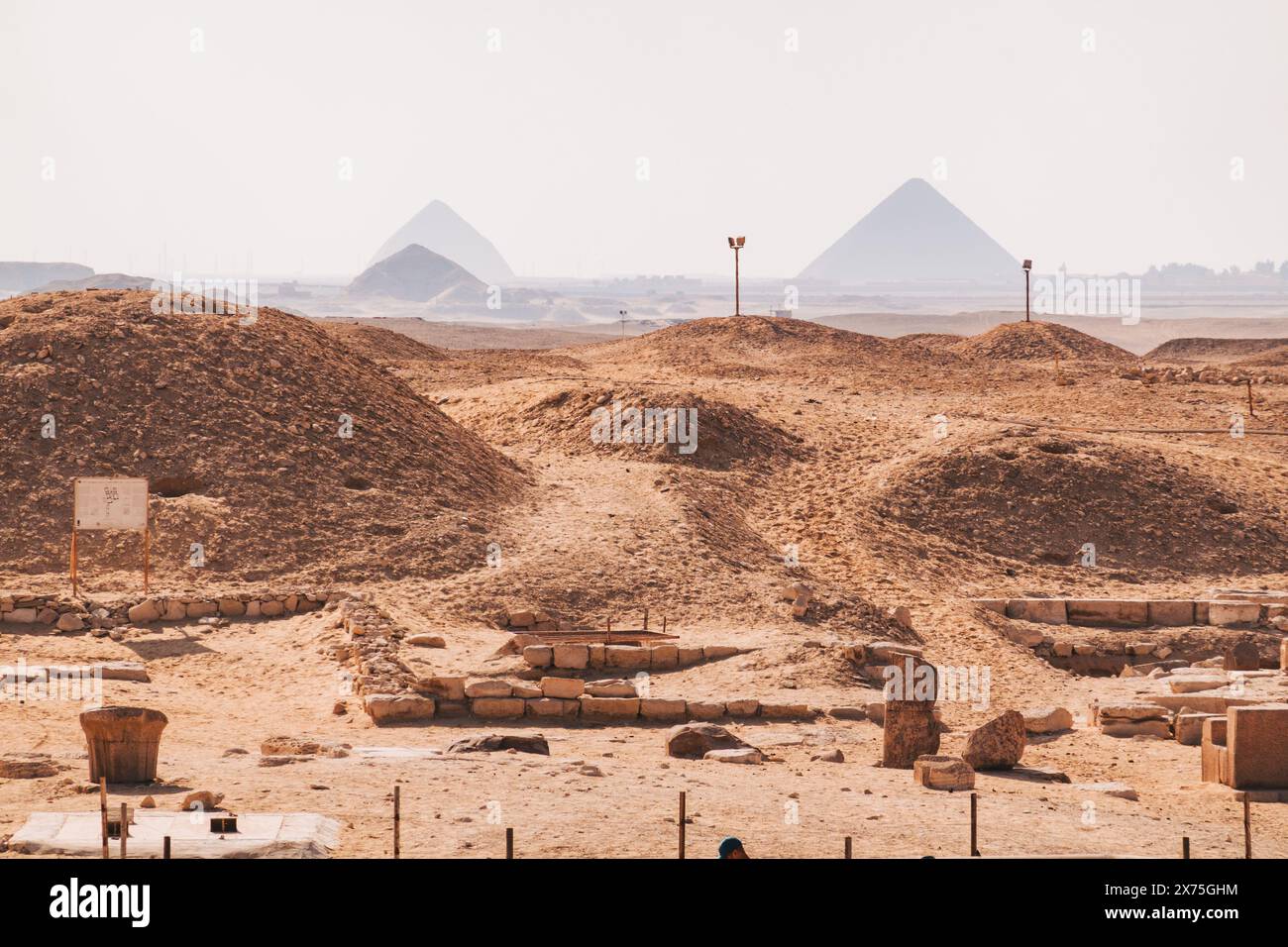 Ruinen in der Nekropolis von Sakkara, mit den Pyramiden von Gizeh, die an einem warmen Tag leicht sichtbar sind Stockfoto