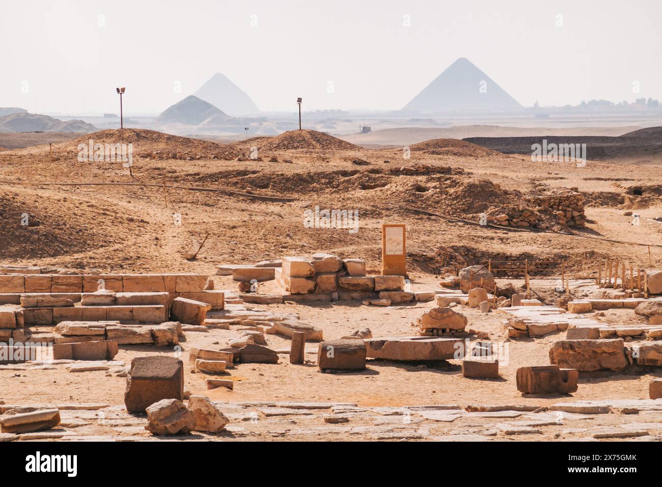 Ruinen in der Nekropolis von Sakkara, mit den Pyramiden von Gizeh, die an einem warmen Tag leicht sichtbar sind Stockfoto