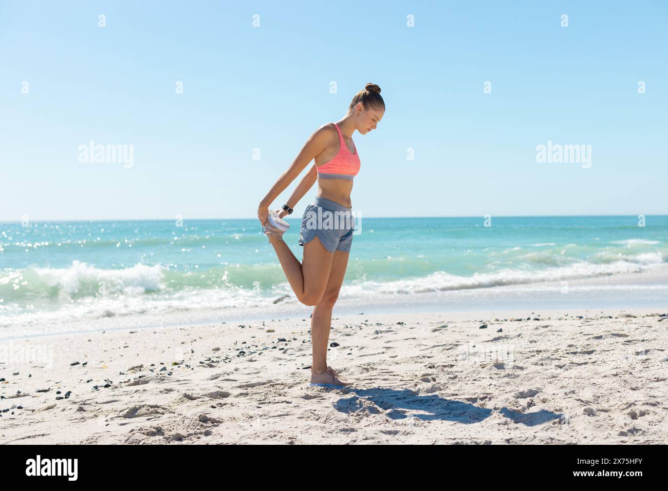 Am Strand dehnt sich eine kaukasische Frau aus, die sportliches Outfit trägt Stockfoto