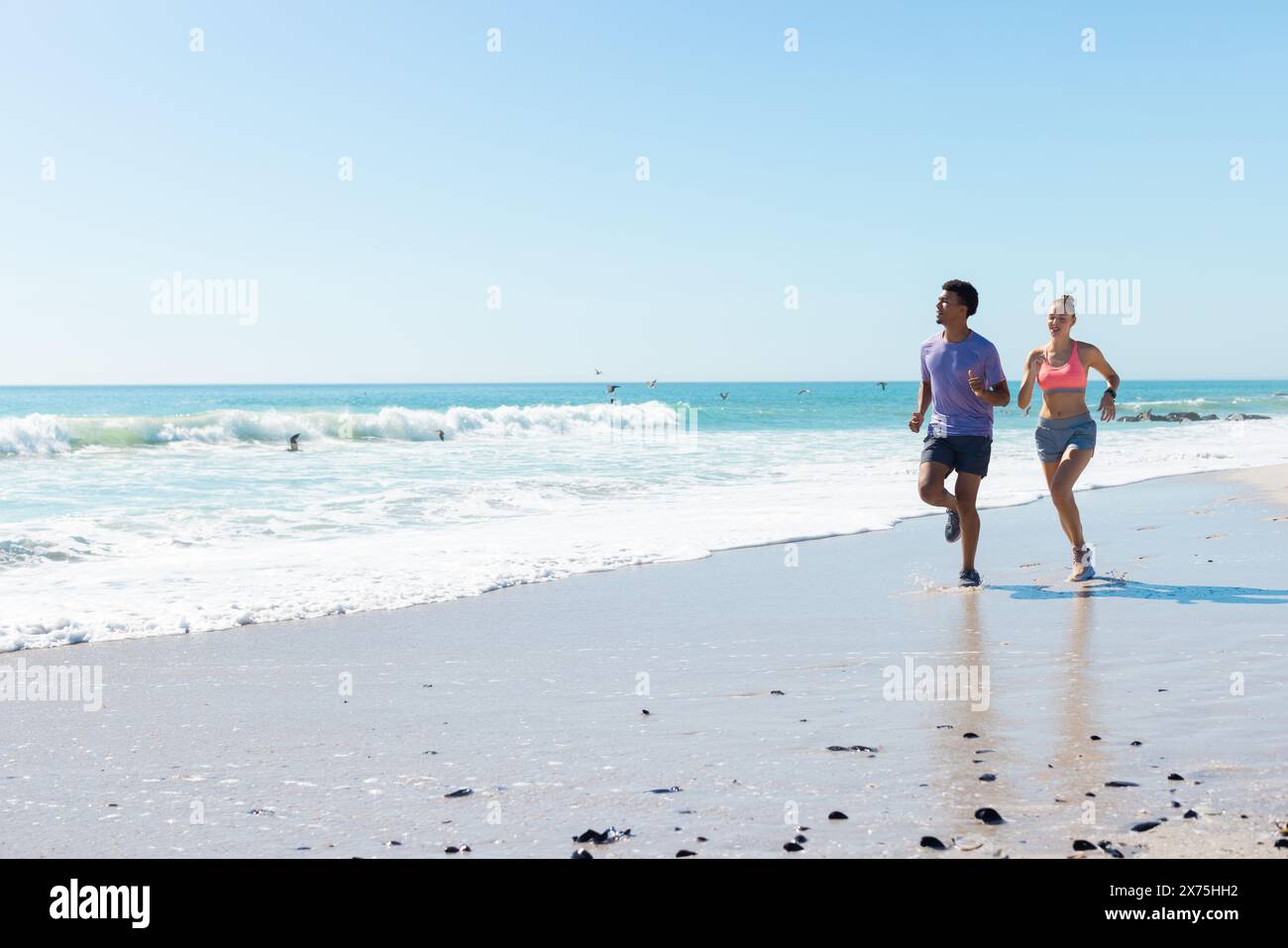 Am Strand laufen diverse Paare unter klarem blauen Himmel Stockfoto