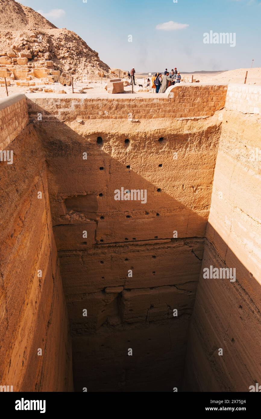 Massiver vertikaler Schacht in der Nekropole von Sakkara, wahrscheinlich Teil einer Grabstätte oder Grabgrabung, mit Besuchern, die von oben unter der Wüste beobachten Stockfoto