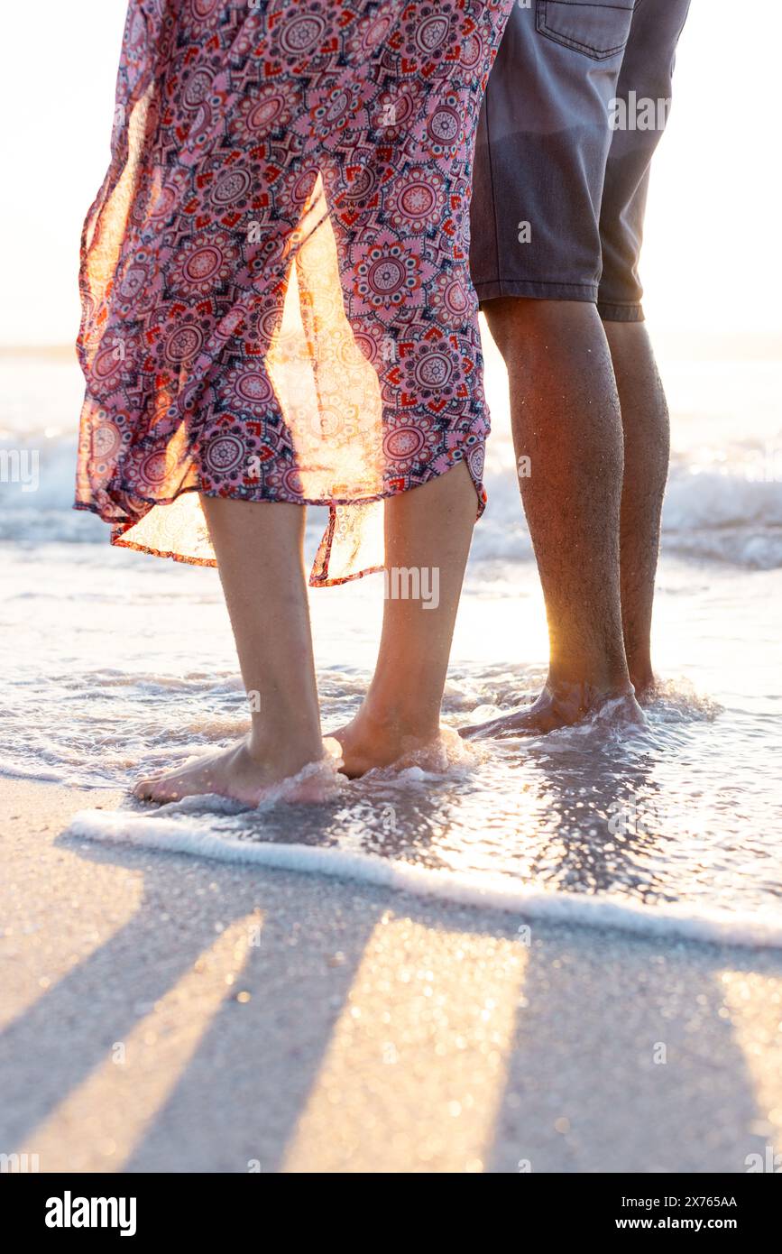 Am Strand stehen zwei rassische Paare im Meer und genießen den Sonnenuntergang Stockfoto