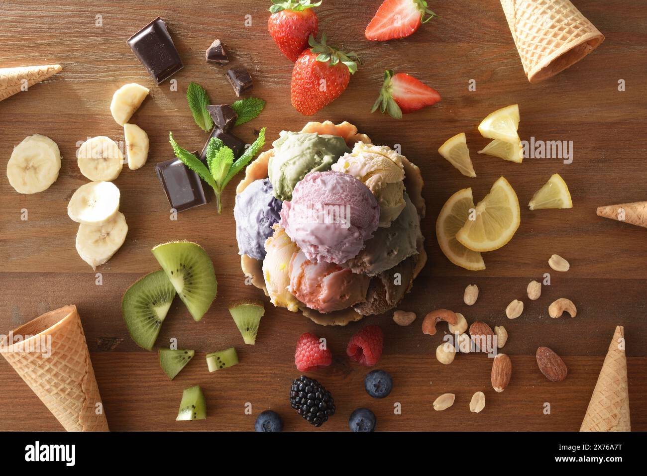Verschiedene Eiskugeln auf Waffelglas auf Holztisch voller Zutaten und Zapfen. Draufsicht. Stockfoto