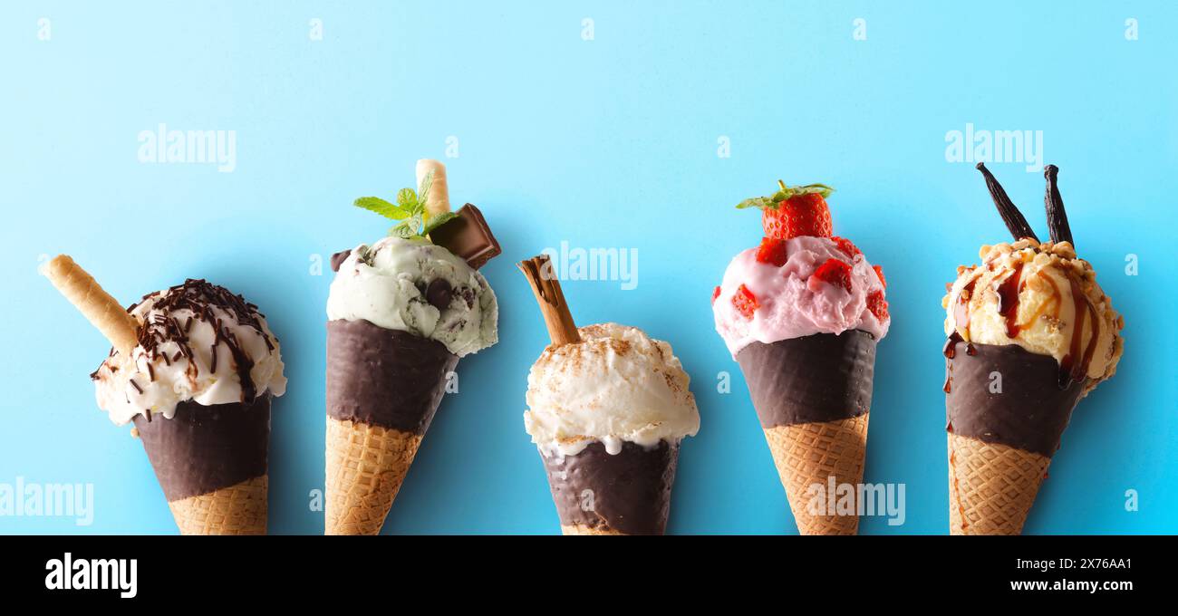 Fünf Eiskegel mit verschiedenen Geschmacksrichtungen hintereinander mit Schokoladenkegel auf blauem Hintergrund. Stockfoto