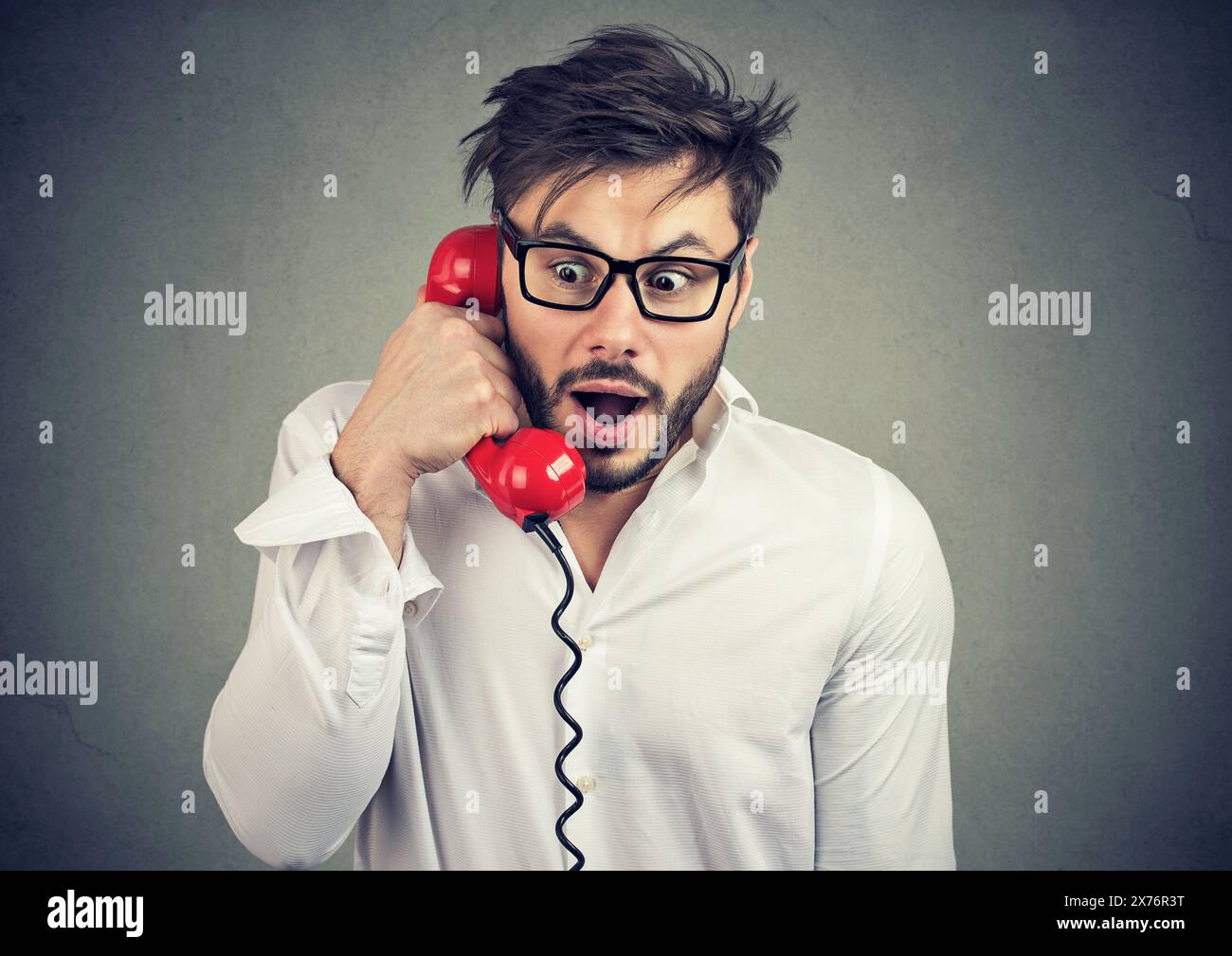 Überraschter junger Mann, der schockierende Nachrichten am Telefon hört Stockfoto