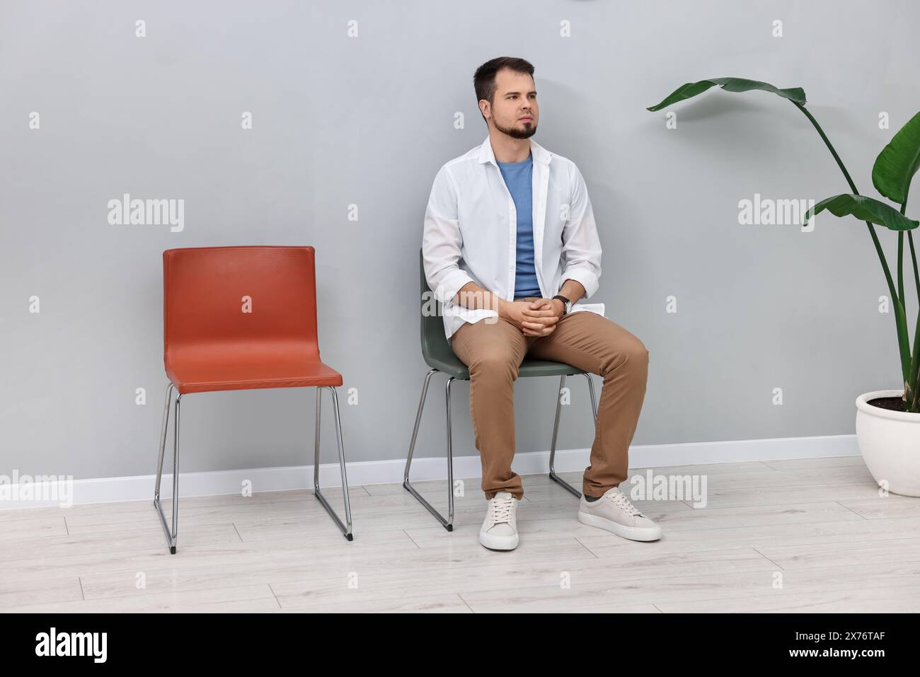 Mann sitzt auf einem Stuhl und wartet drinnen auf einen Termin Stockfoto