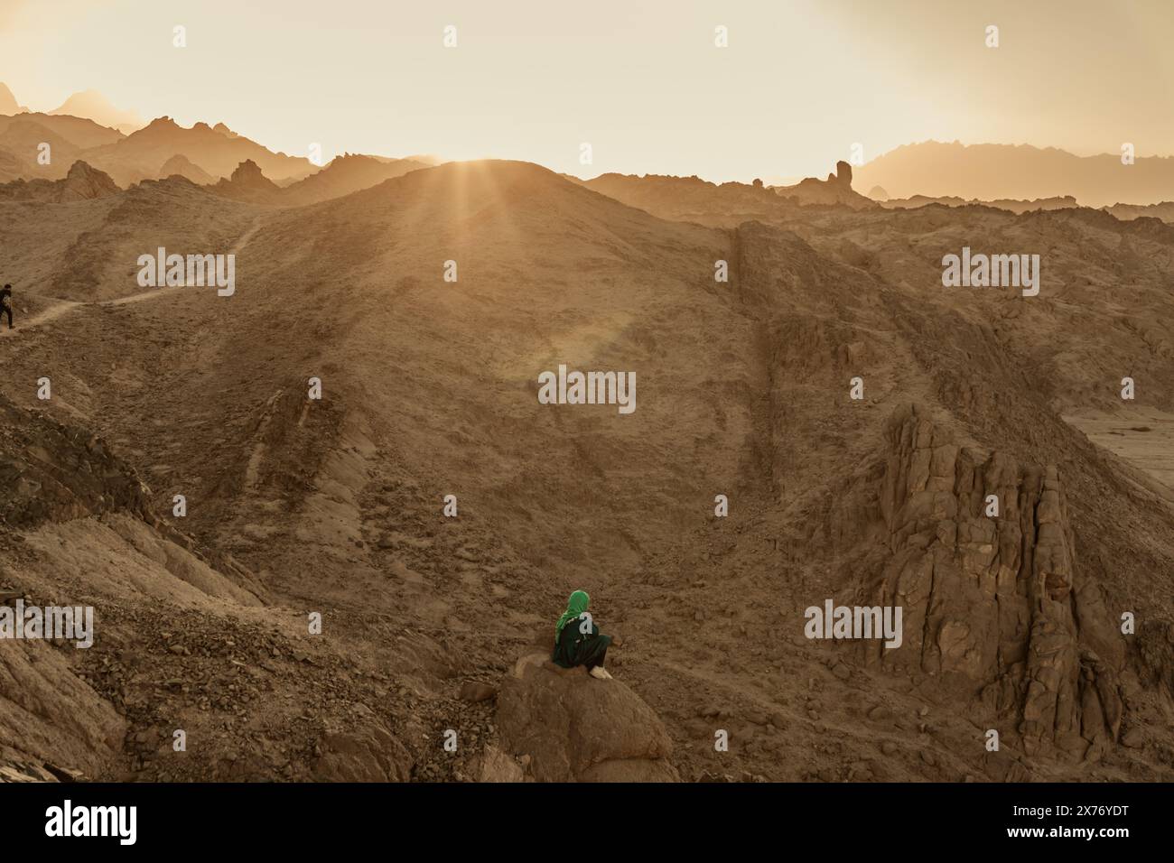 Das verhüllte junge Mädchen sitzt in der Abenddämmerung allein in der zerklüfteten Felsenlandschaft Stockfoto