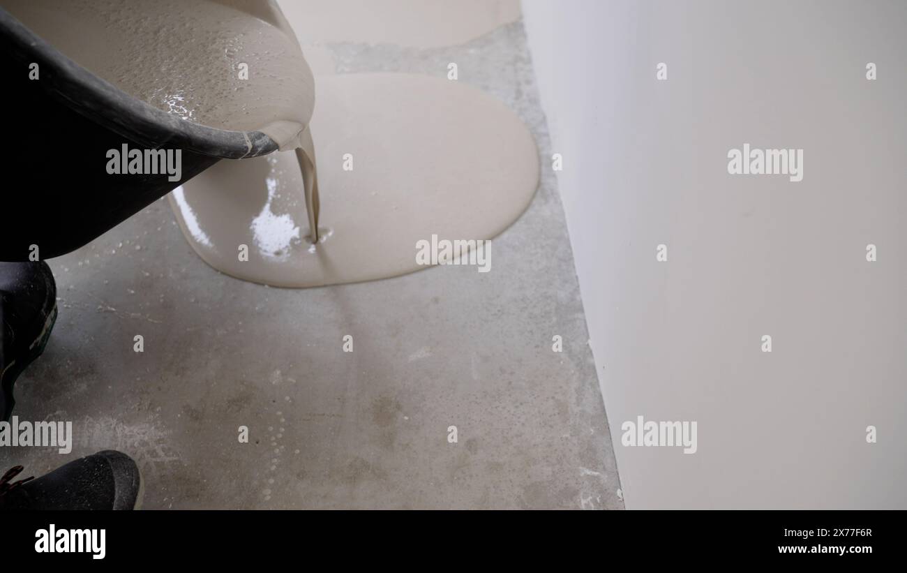 Arbeiter gießen selbstnivellierenden Boden aus. Ausgießen Von Selbstnivellierenden Böden. Selbstnivellierende Böden auf Einer großen Fläche, Ein Arbeiter. Selbstnivellierendes Epoxid. Nivellierung mit einem Stockfoto