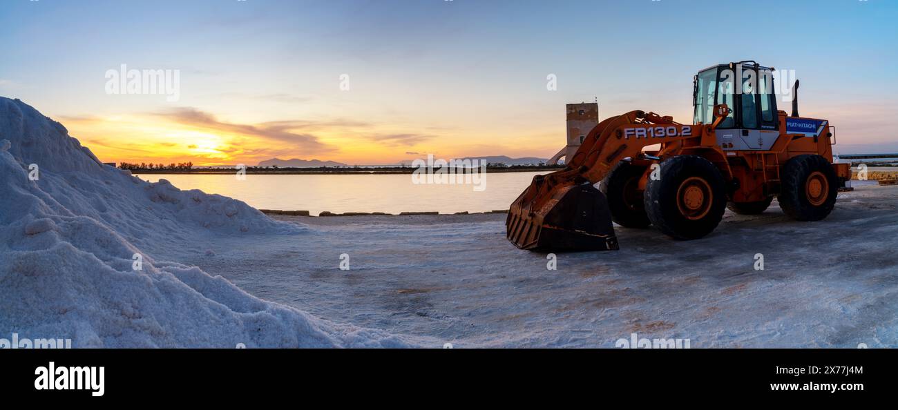 Paceco, Italien - 3. Januar 2024: Frontlader und Seesalzhaufen in der Salzebene von Trapani und Paceco bei Sonnenuntergang Stockfoto