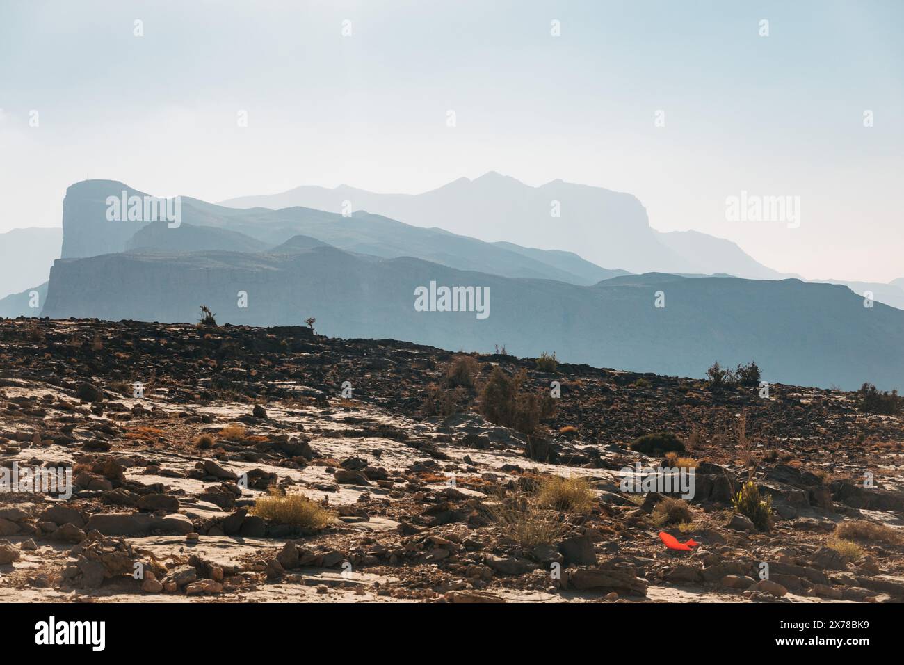 In Jebel Shams, Oman, verblassen sich mehrschichtige Bergsilhouetten in den trüben Horizont, mit felsigem Gelände im Vordergrund unter hellem Himmel. Stockfoto