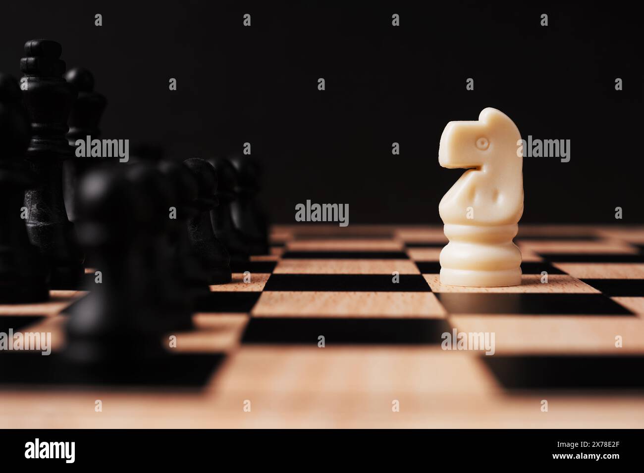 Weißes Ritterschach steht vor einer Reihe von schwarzem Schach mit schwarzem Hintergrund Stockfoto