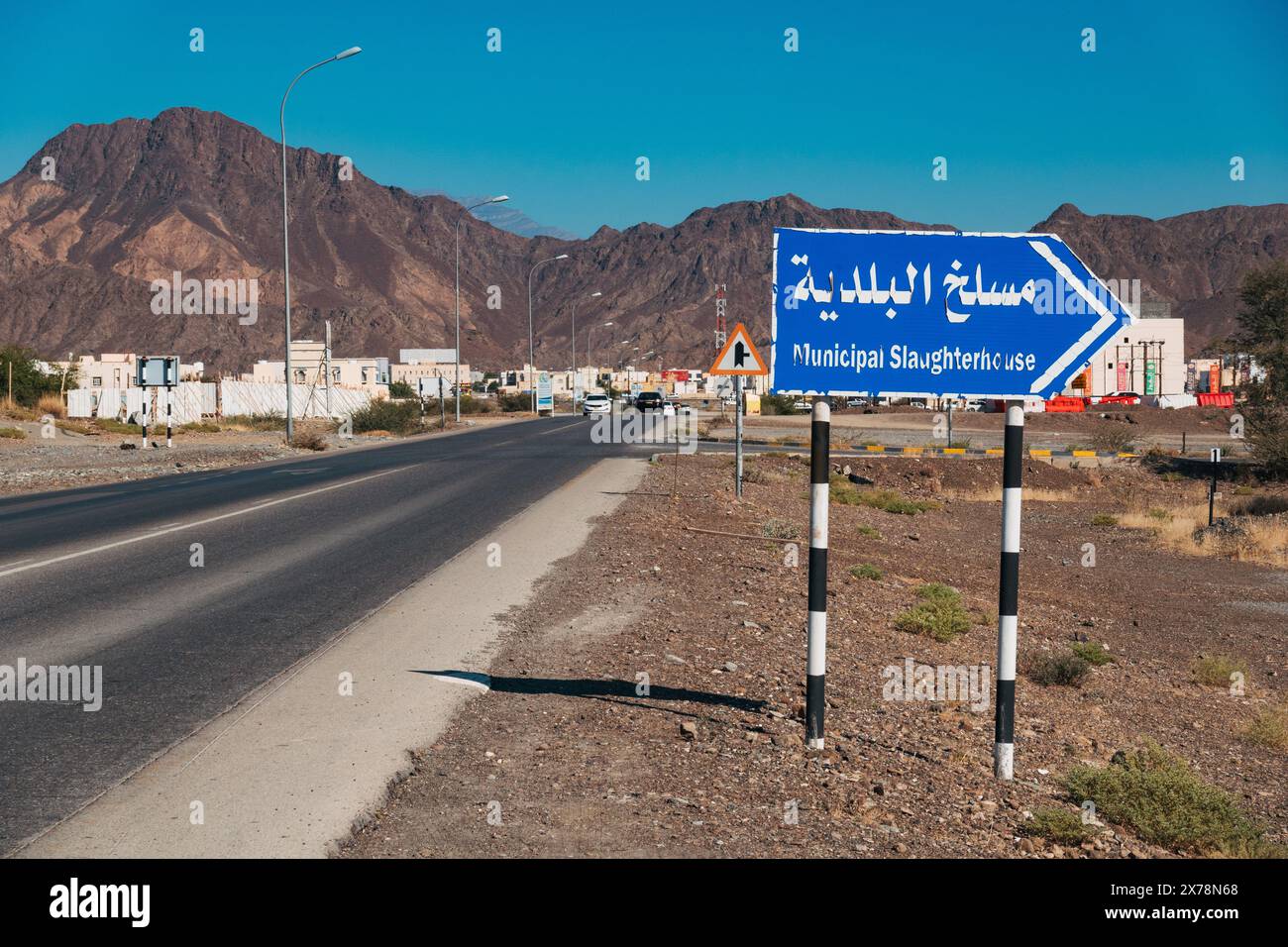 Straßenschild zum städtischen Schlachthof in Bahla, Oman, mit Wüstenlandschaft, Bergen und einem klaren blauen Himmel Stockfoto