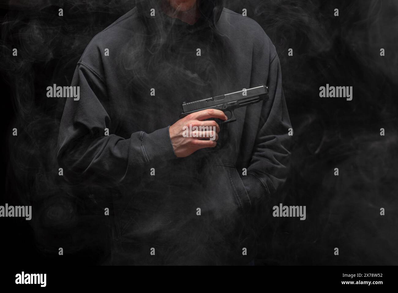 Junger Mann in einem schwarzen Hoodie mit einer Pistole auf einem rauchigen schwarzen Hintergrund Stockfoto