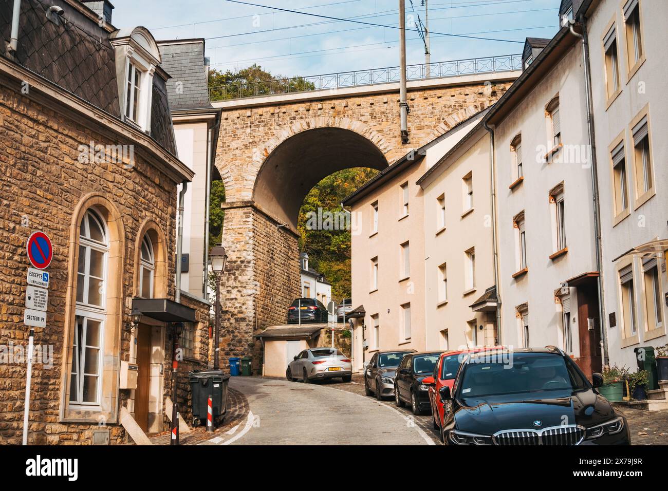 Eine malerische Straße in Luxemburg-Stadt mit geparkten Autos, Wohnhäusern und einer steinernen Eisenbahnbrücke, die sich über den Apartments erhebt Stockfoto
