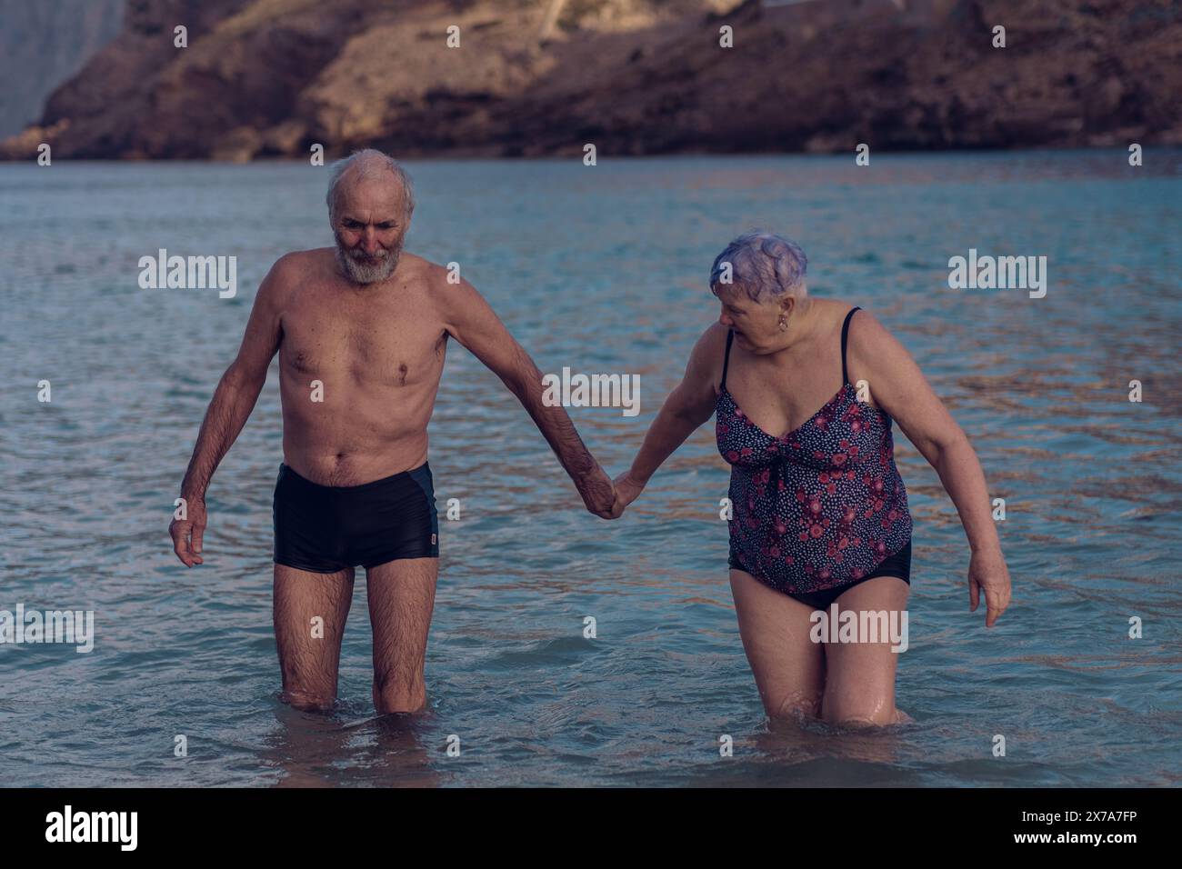 Alte Leute schwimmen im Meer. Ein älteres Paar genießt das Leben, indem es Zeit auf See verbringt. Ein alter Großvater und eine Großmutter im Badeanzug gehen entlang Stockfoto