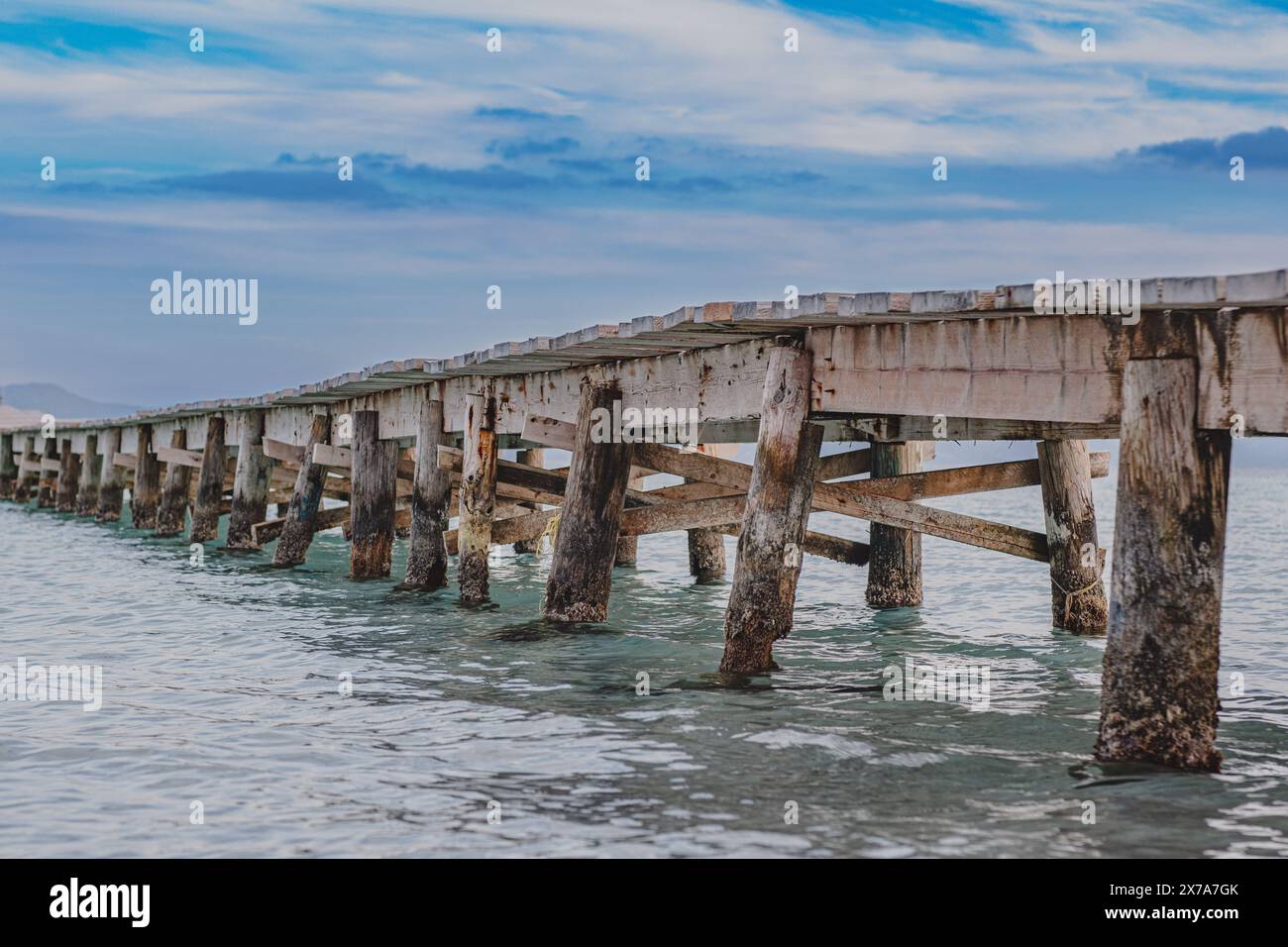 Foto eines hölzernen Piers, der sich ins Meer erstreckt. Schöne Seitenansicht auf den Pier. Ruhiges türkisfarbenes Meerwasser, hölzerne Brückenstruktur und wunderschöner Himmel. Stockfoto