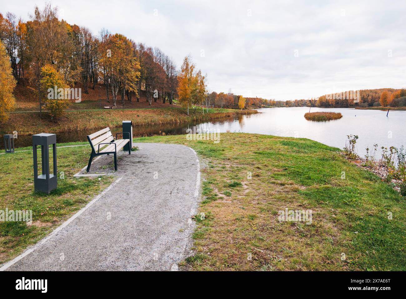 Ein Wanderweg und eine Parkbank neben einem See an einem ruhigen Herbsttag in der Stadt Plungė, Litauen Stockfoto