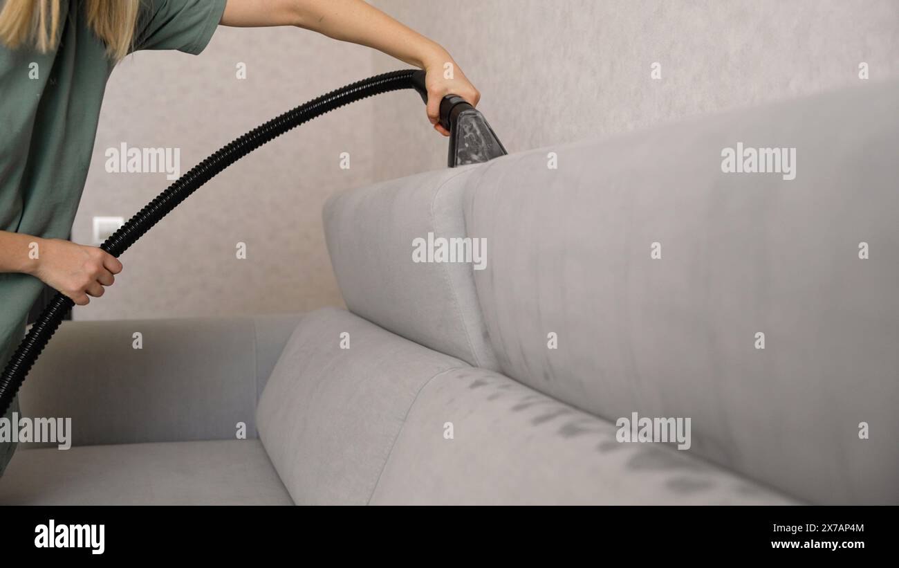 Nahaufnahme einer nicht erkennbaren Frau mit Handschuhen, die ein schmutziges Sofa mit einem Polster-Trockenreinigungsabzieher reinigt. Reinigungsservice bei Stockfoto