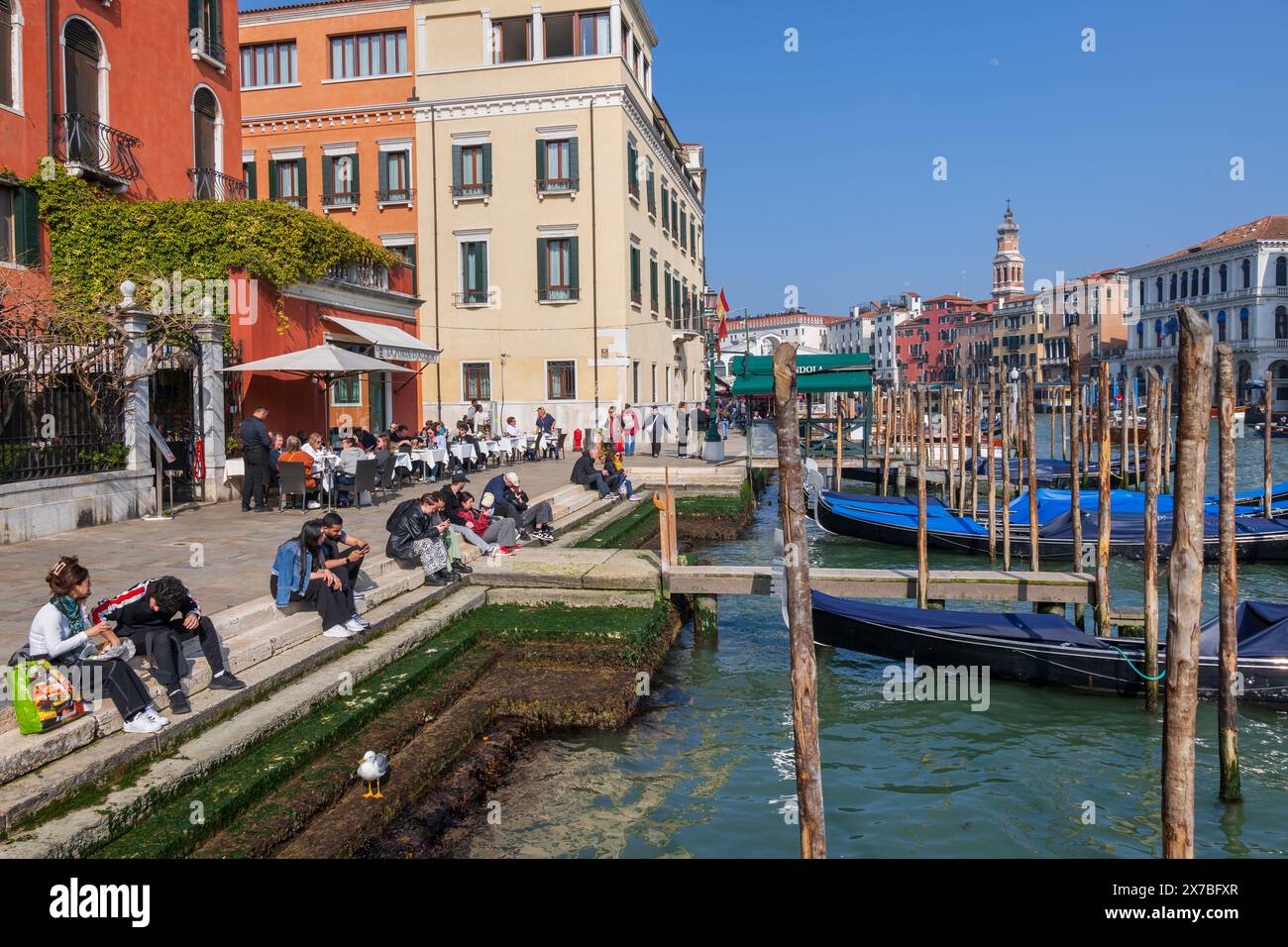 Stadt Venedig, Italien, die Menschen entspannen sich am Canale Grande Riva del Vin mit ihren vertäuten Gondeln im Viertel San Polo, in der Nähe der Rialto-Brücke. Stockfoto